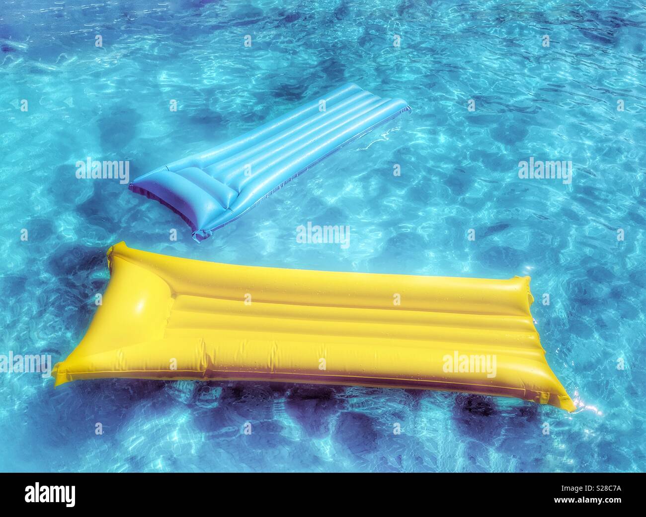 Giallo e blu di materassini gonfiabili floating in blu piscina Foto Stock