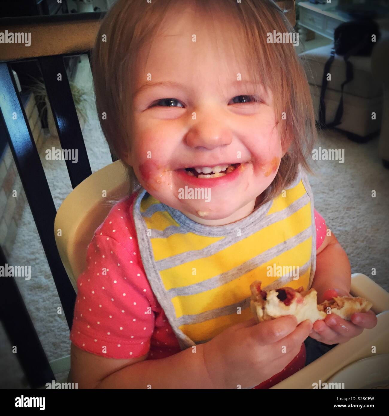 Baby girl felicemente mangiando un burro di arachidi e jelly sandwich con gran parte di essa sul suo volto, STATI UNITI D'AMERICA - Immagine stock catturata con smartphone