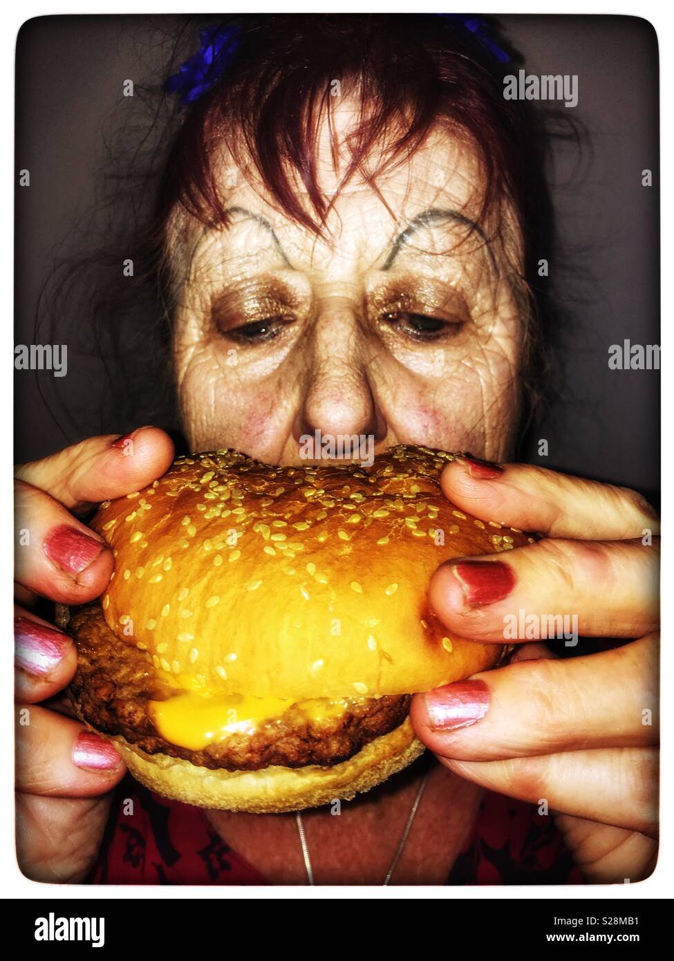 Donna anziana di mangiare un hamburger formaggio Foto Stock
