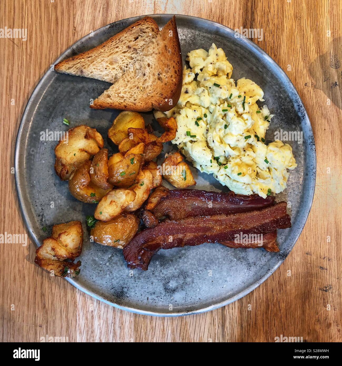 Una vista in pianta di una prima colazione a base di uova strapazzate, bacon, patate e toast su un rustico di piastra metallica Foto Stock