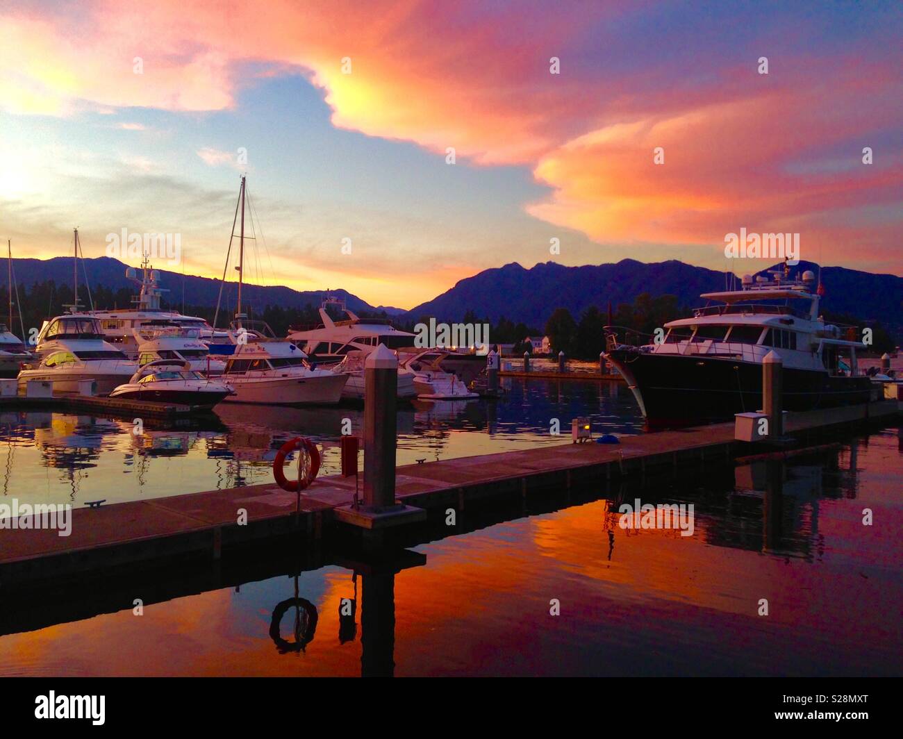 Marina di Coal Harbour in Vancouver al tramonto con le barche a vela e le montagne dietro il mare in Canada - Immagine stock catturata con smartphone