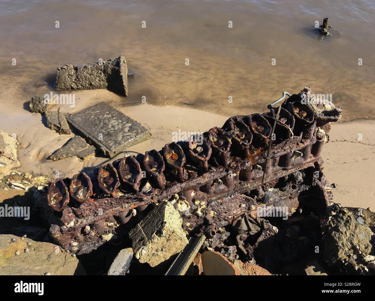Un estremamente rusty blocco motore, giacente nella sabbia in corrispondenza del bordo di un estuario; il duro ambiente di acqua salata che mostra come la corrosione è grandemente accelerato in tale circostanza. Sicuramente un write-off! Foto Stock
