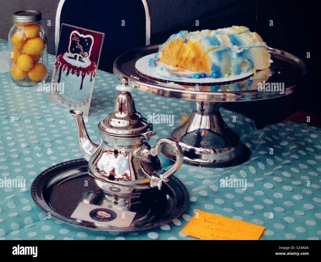 Ancora vita costituito da un vasetto di limoni, teiera in argento e riposare la torta con la torta su aqua polka tovaglia punteggiata Foto Stock