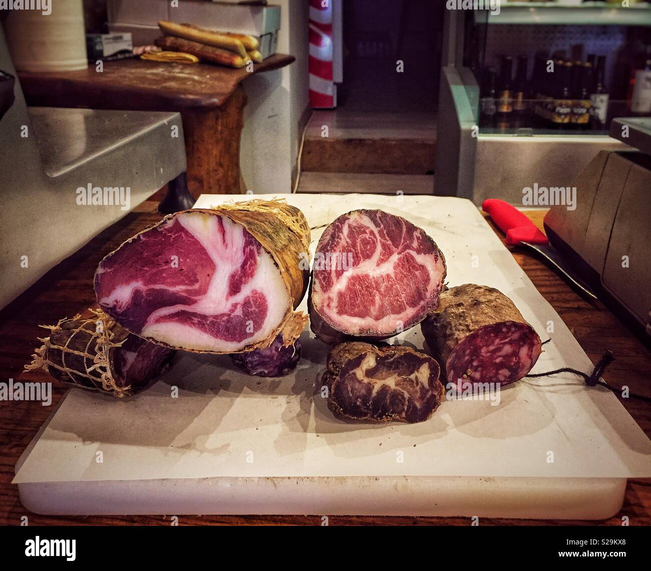 Essiccato, induriti salsicce su un tagliere all'interno di un tradizionale negozio di specialità gastronomiche mediterranee secche di vendita prosciutti, salumi e formaggi. - Immagine stock catturata con smartphone