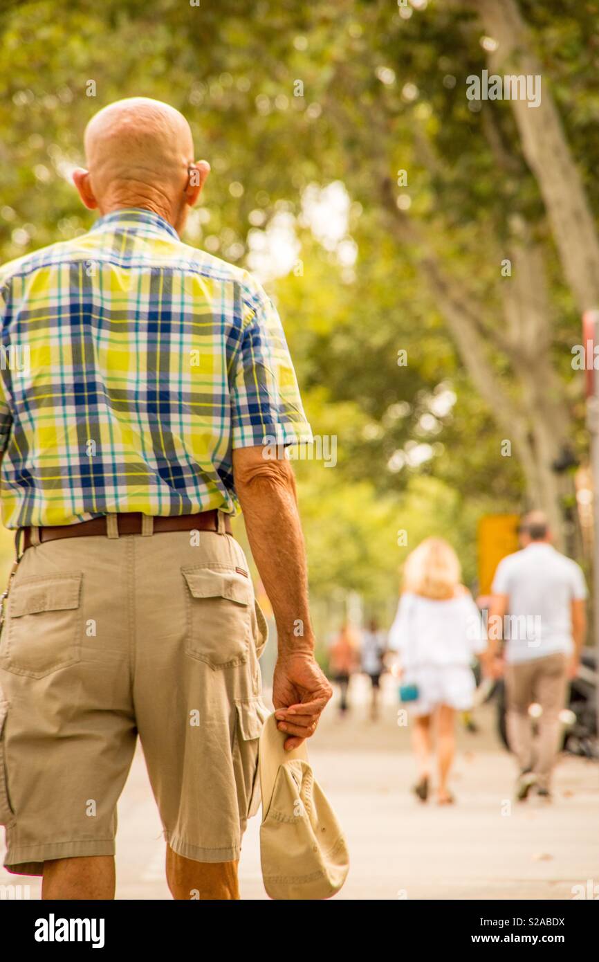 Il vecchio uomo a camminare con il cappello in mano in città a caldo giorno d'estate Foto Stock