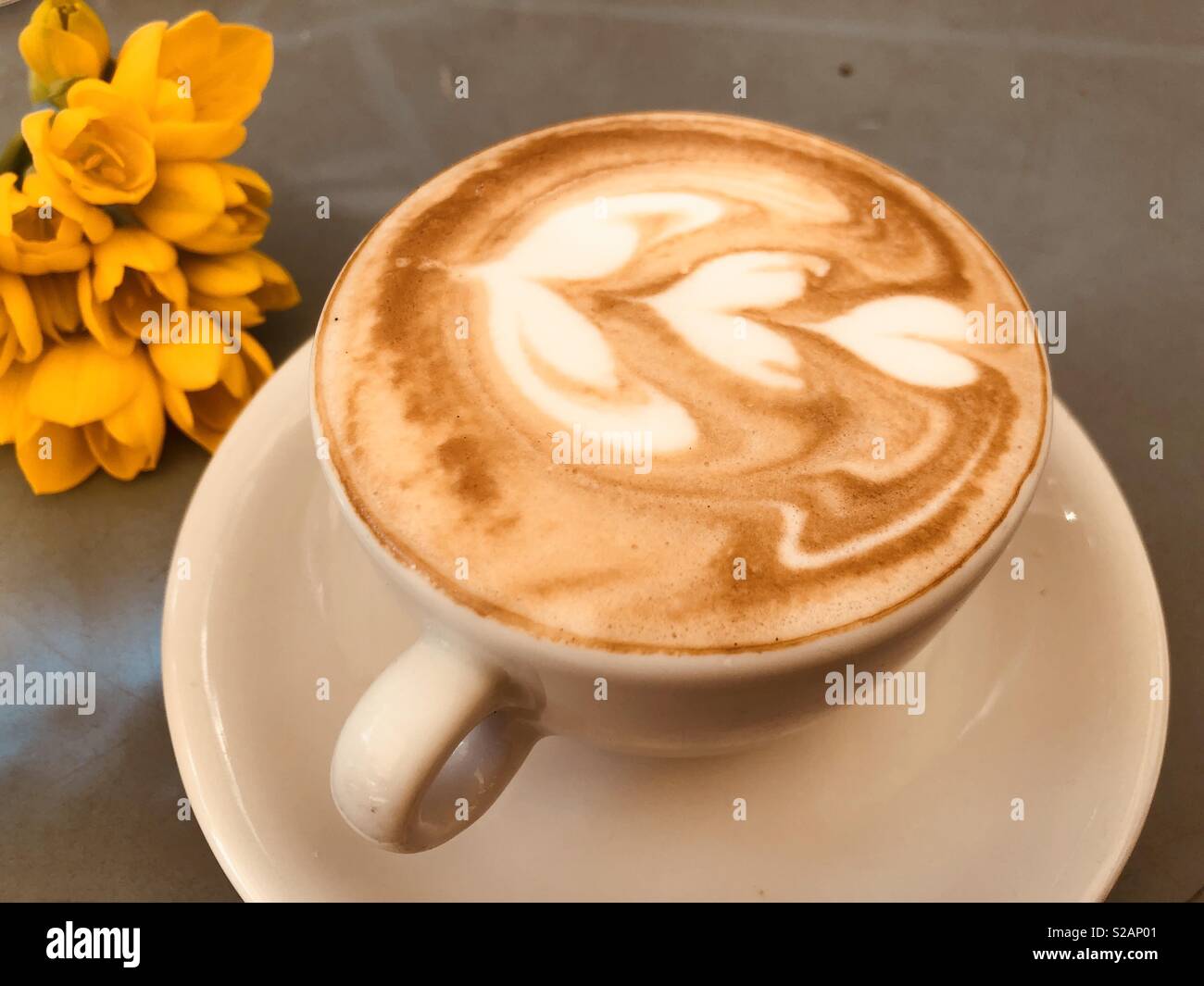 Una tazza di modellato piatto bianco e fiori di colore giallo Foto Stock