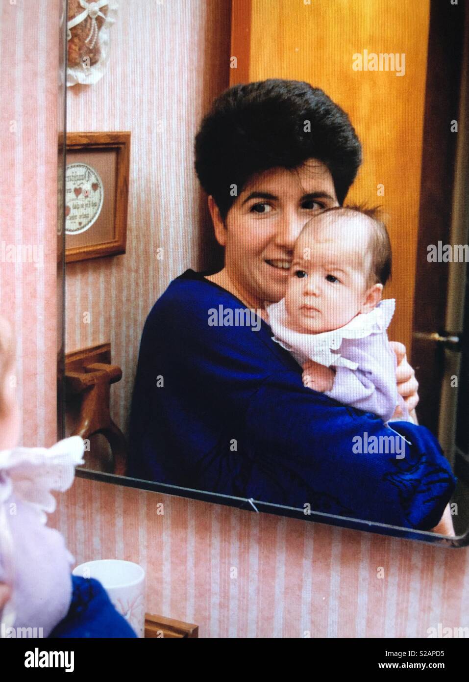 Una madre detiene una bambina di fronte ad uno specchio per vedere la sua riflessione Foto Stock