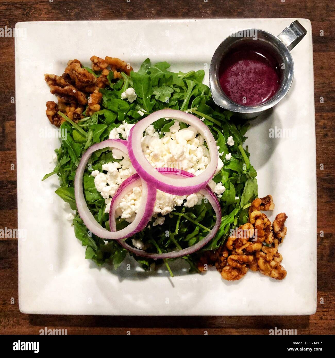 Un insalata con formaggio, le noci e le cipolle su un quadrato bianco piastra - Immagine stock catturata con smartphone