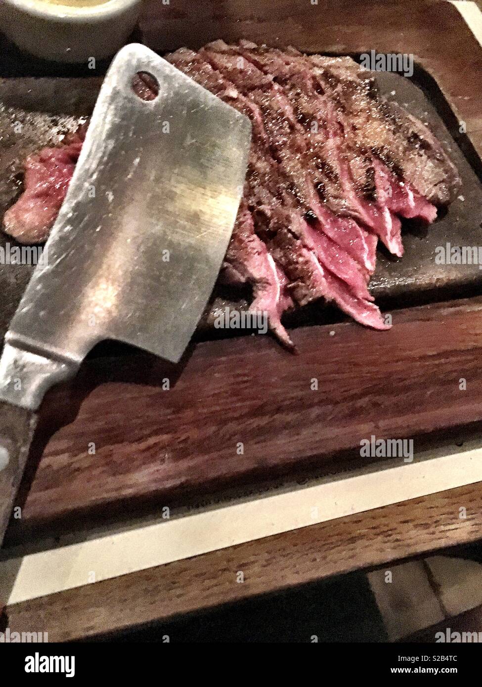 Bistecca cotta rari servita con un macellaio cleaver su sfrigolanti padella di ferro in ferro piatto di Henrietta Street restaurant Londra Foto Stock