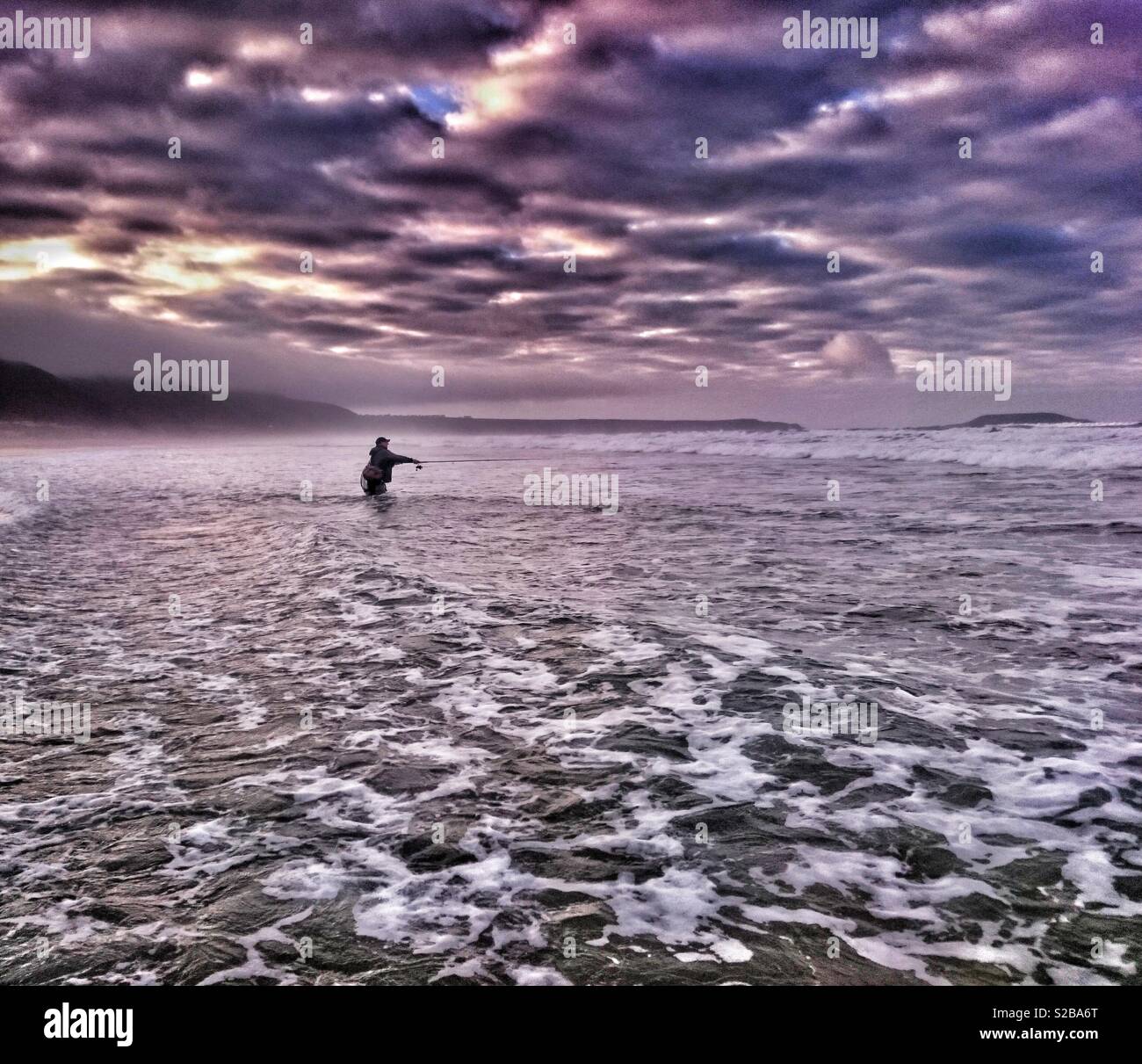 Il pescatore pesca nel surf per bass a Llangennith beach, Gower, Galles. Foto Stock
