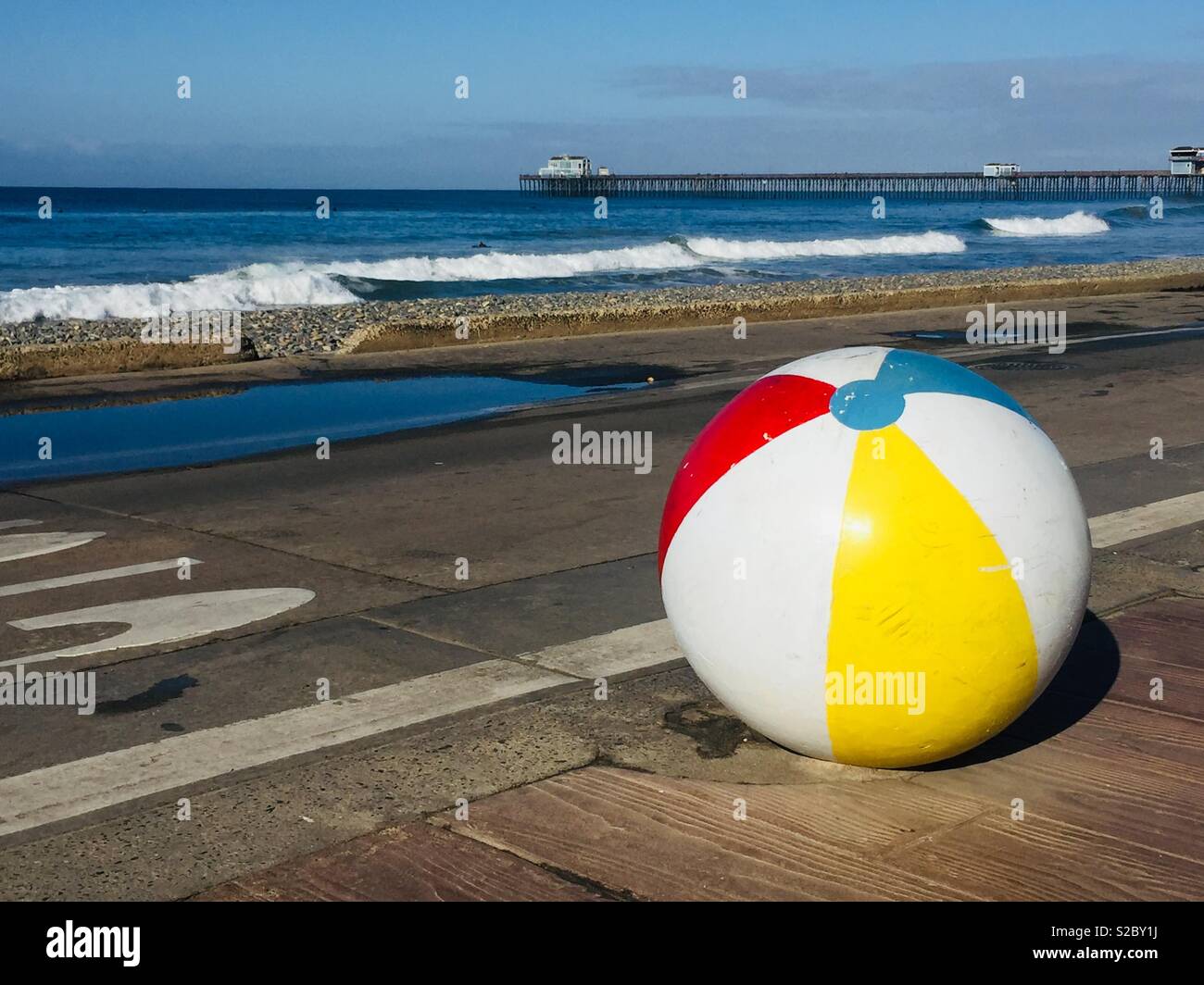 Una vista panoramica dell'Oceanside, California pier dal parco pubblico da spiaggia. Un simpatico, colorato barriera di cemento dipinta come una palla spiaggia è in primo piano. Foto Stock