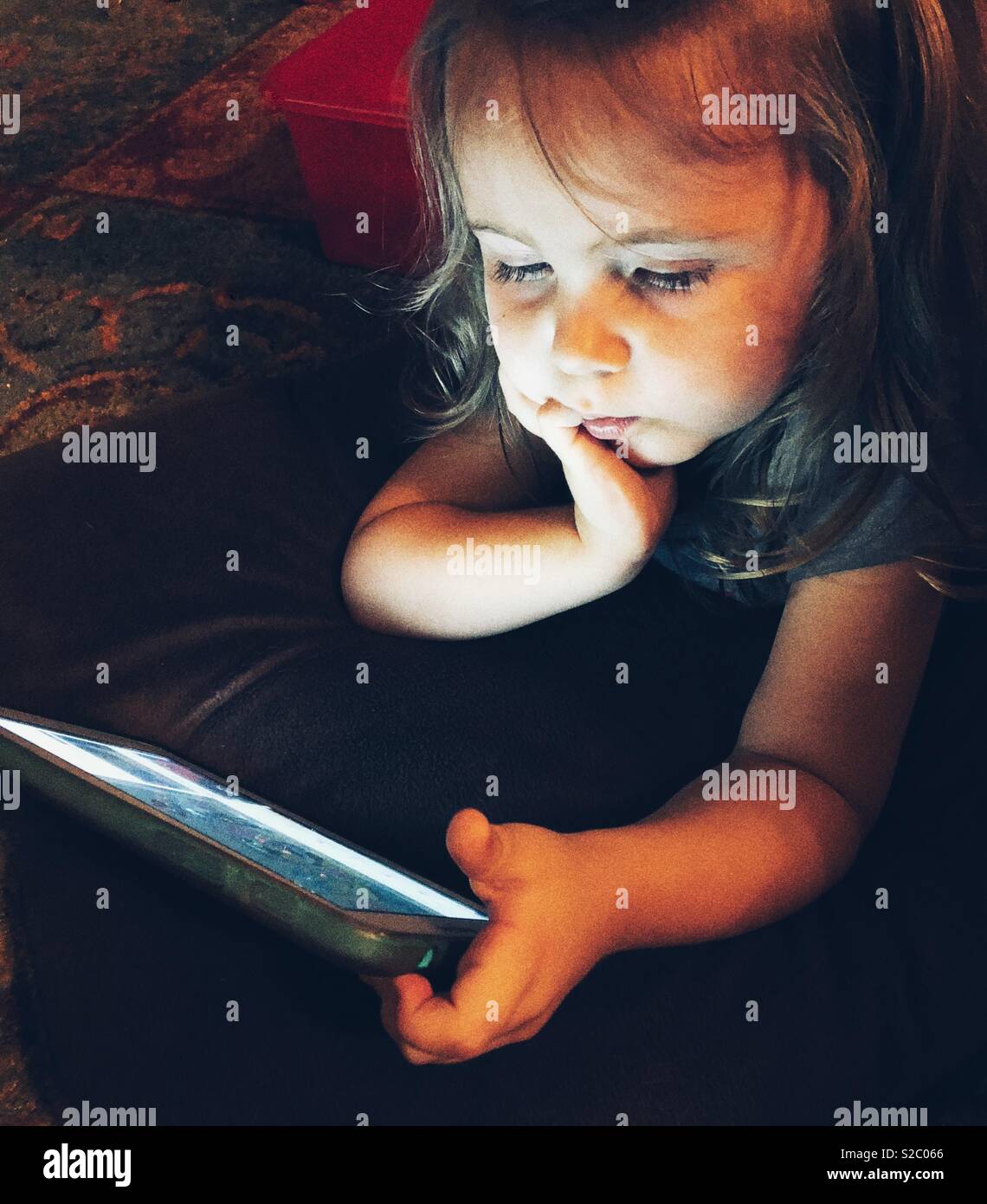 Il Toddler girl posa sul pavimento al buio a giocare con i tablet - Immagine stock catturata con smartphone