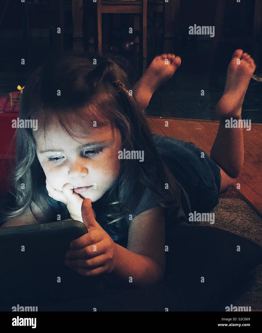 Il Toddler girl posa sul pavimento durante la notte con una pastiglia illuminare il suo volto - Immagine stock catturata con smartphone