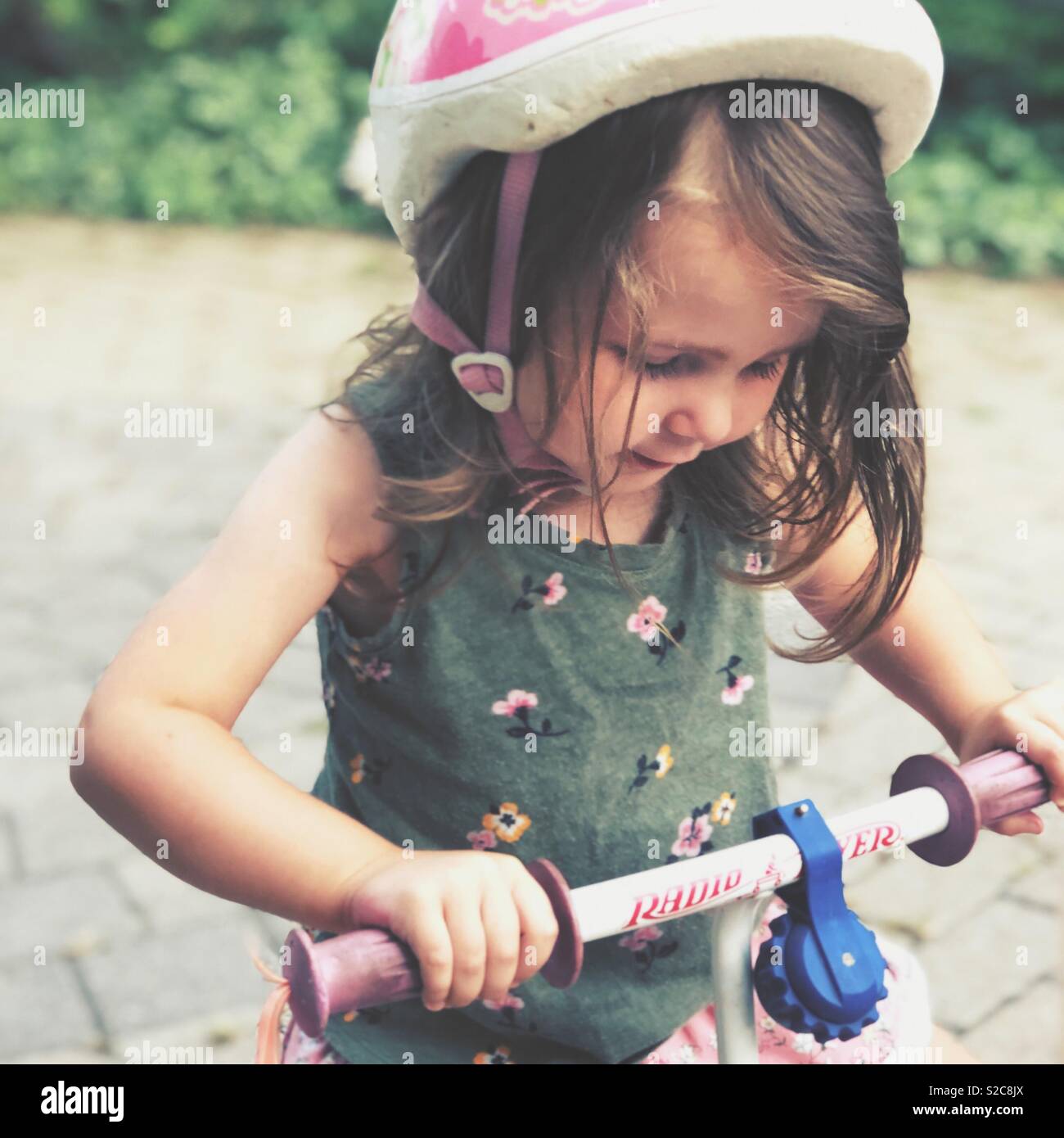 Bimbi felici ragazza indossando mountain bike e casco rosa di equitazione Radio Flyer triciclo al di fuori Foto Stock