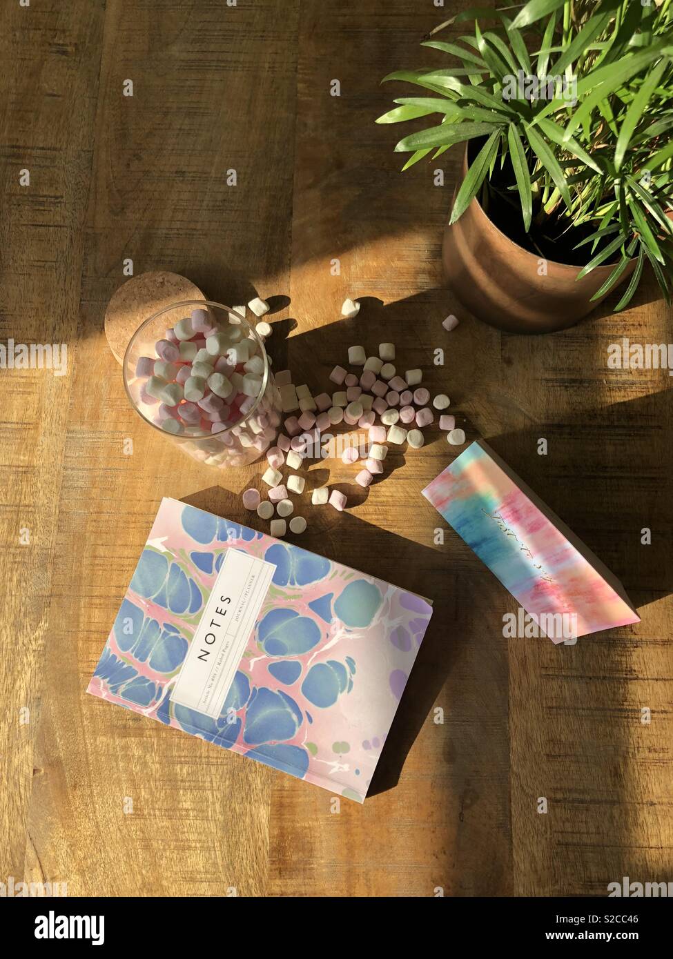 Desk laici piatta con mini marshmallow prelibatezze dolci, marmo notebook modellato e biglietto di auguri. Impianto di pentola in angolo Foto Stock
