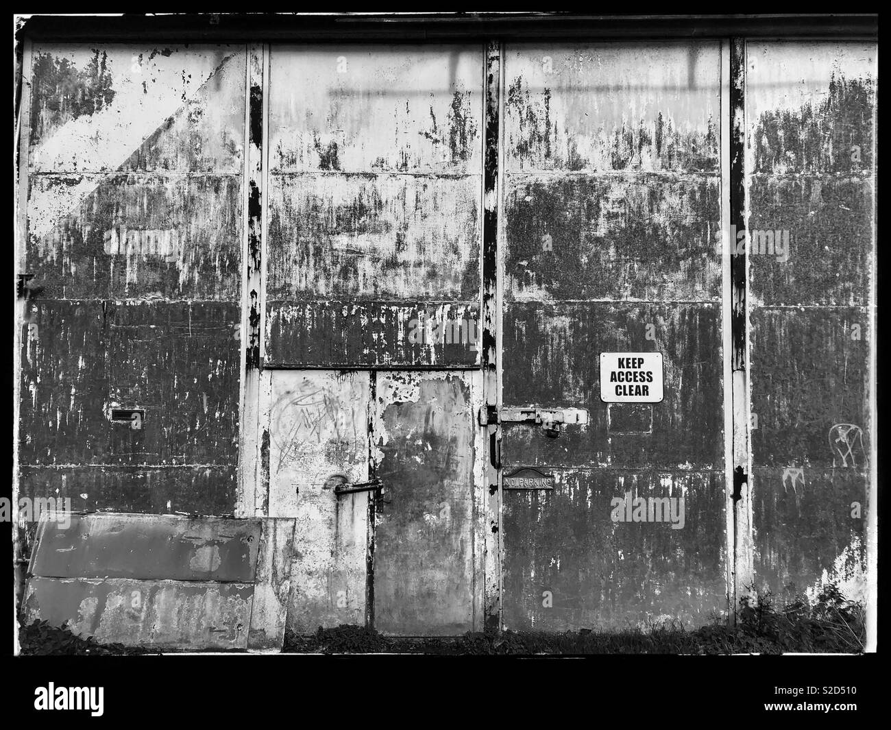 Vecchia porta in officina o in un magazzino con pareti scrostate. In bianco e nero. Foto Stock
