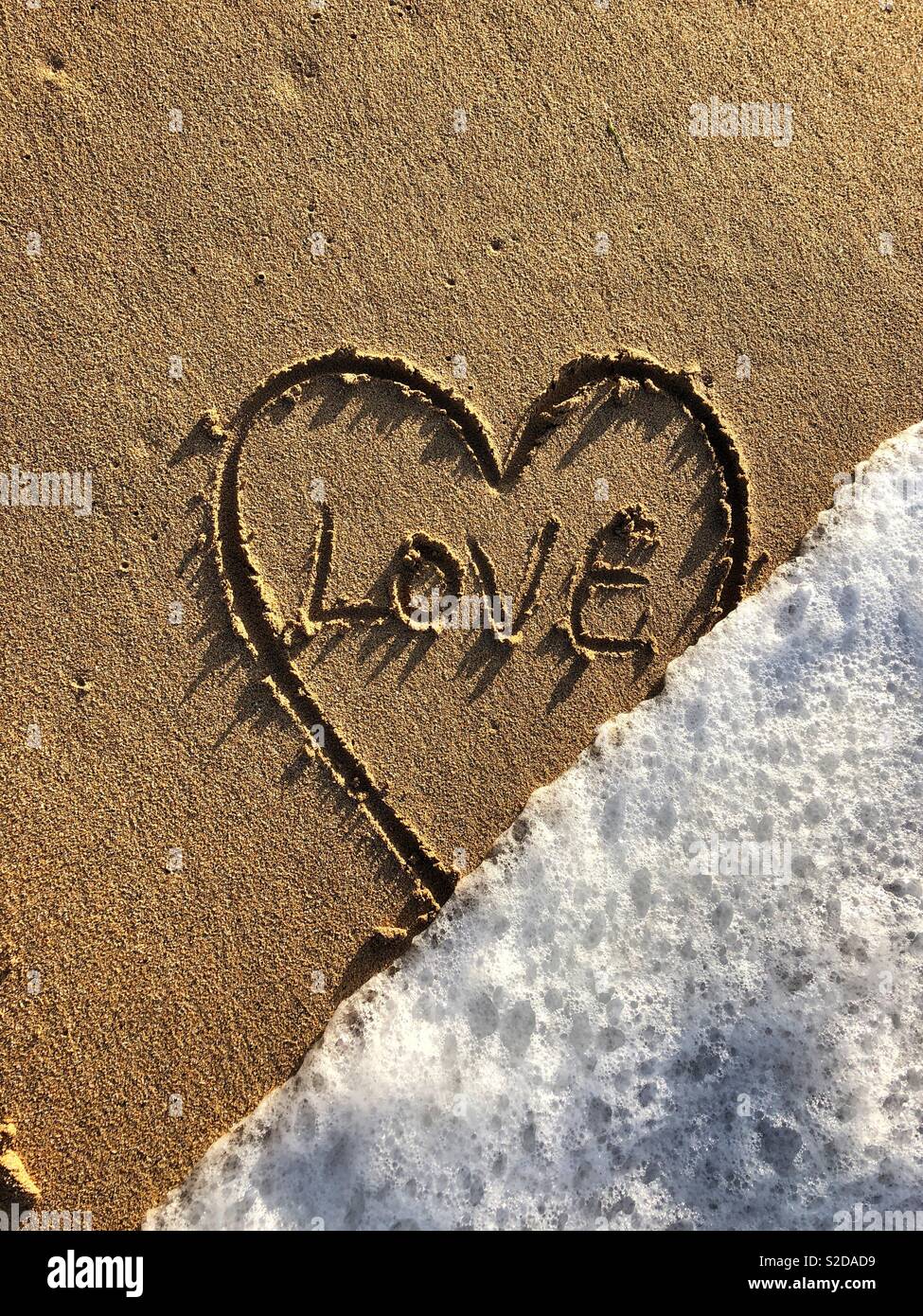 Cuore d'amore nella sabbia di essere lavati via dalla marea. Foto Stock