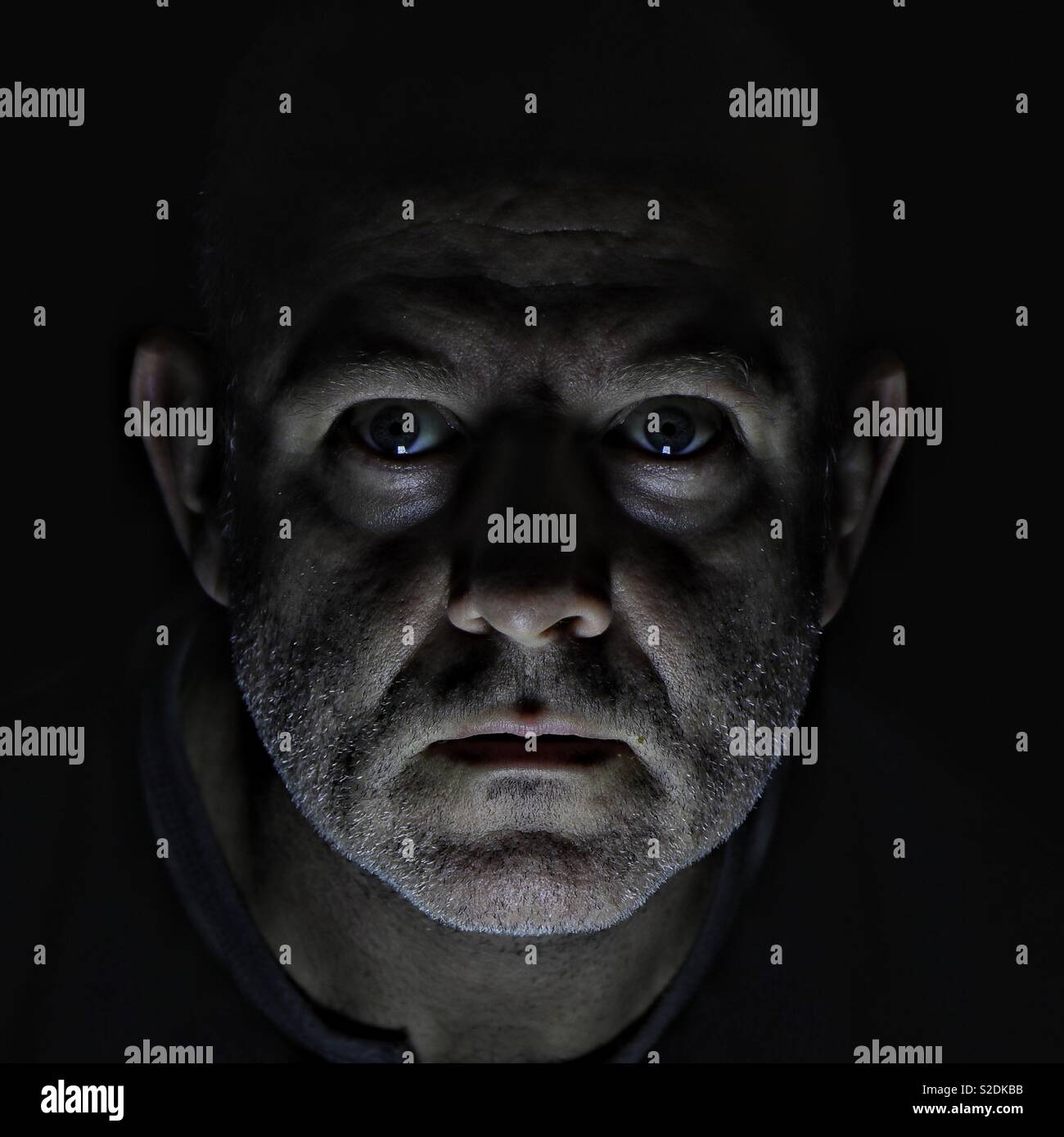 Un ritratto drammatico e inquietante di un uomo in condizioni di scarsa illuminazione, con ombre profonde e un'espressione intensa che evoca sentimenti di mistero, paura e suspense Foto Stock Un ritratto drammatico e inquietante di un uomo in condizioni di scarsa illuminazione, con ombre profonde e un'espressione intensa che evoca sentimenti di mistero, paura e suspense Foto Stock