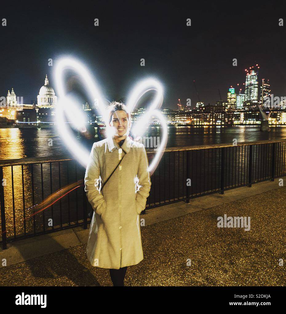 Giovane donna in piedi sulla banca del sud nelle ore notturne a Londra con ante dipinte dietro di lei con la luce. - Immagine stock catturata con smartphone