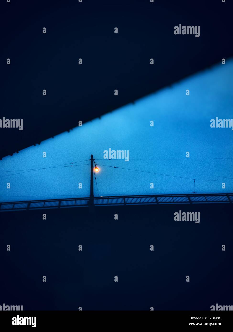 Singola lampada di strada sul ponte contro il cielo blu scuro al crepuscolo, fotografata da sotto. - Immagine stock catturata con smartphone