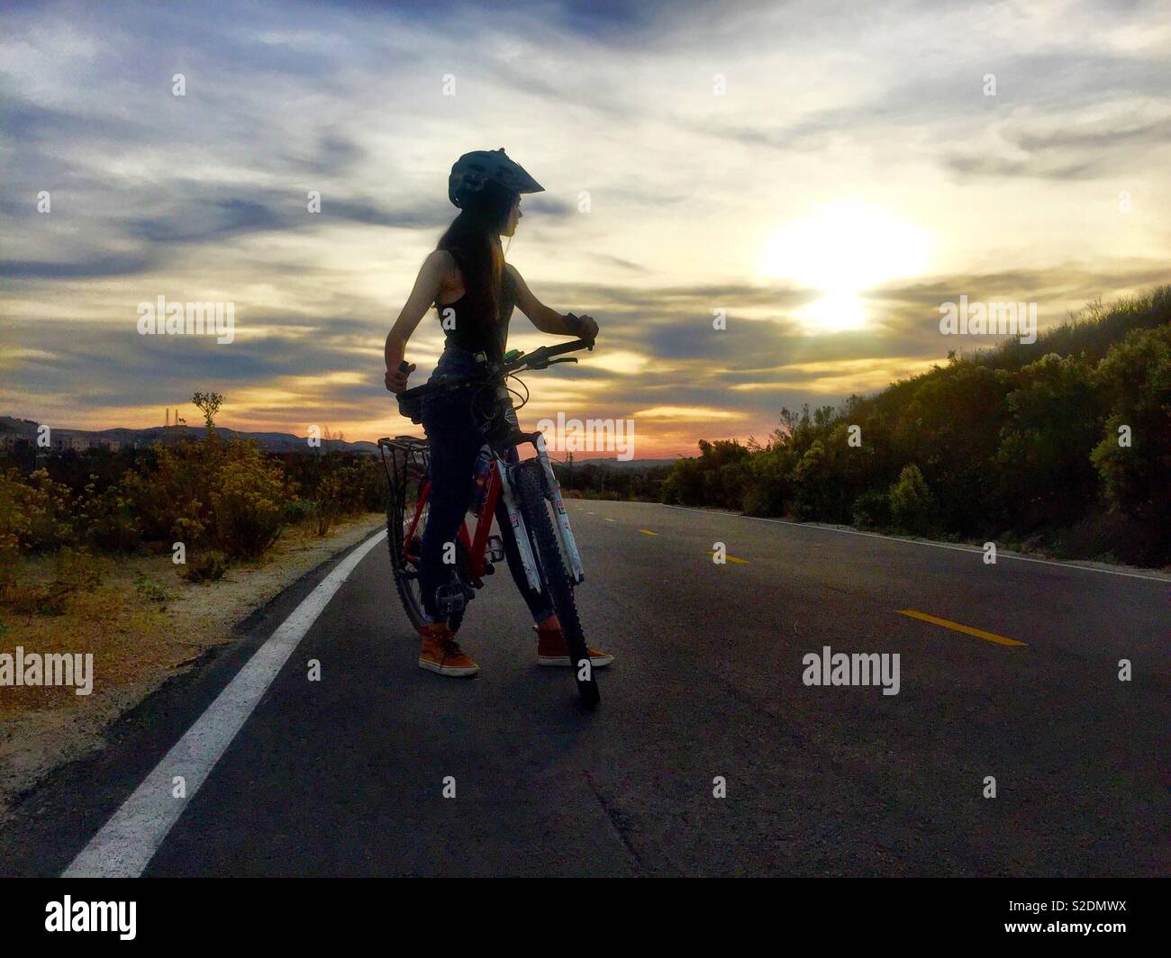 Una ragazza adolescente in sella ad una bici si stagliano contro un tramonto nella California Meridionale. Foto Stock