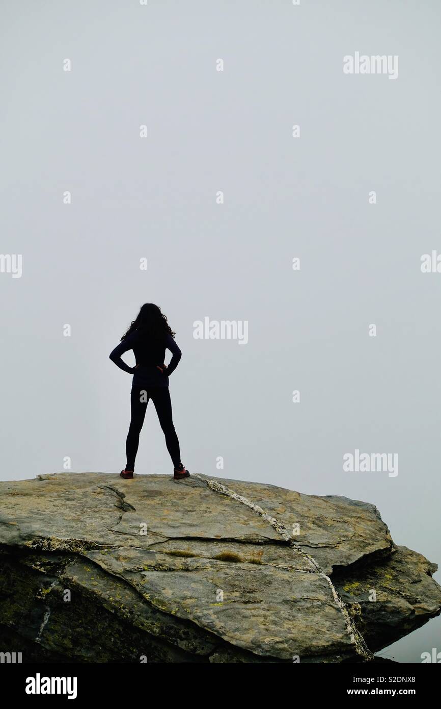 Donna forte in piedi in una roccia fino in montagna a guardare le nuvole Foto Stock