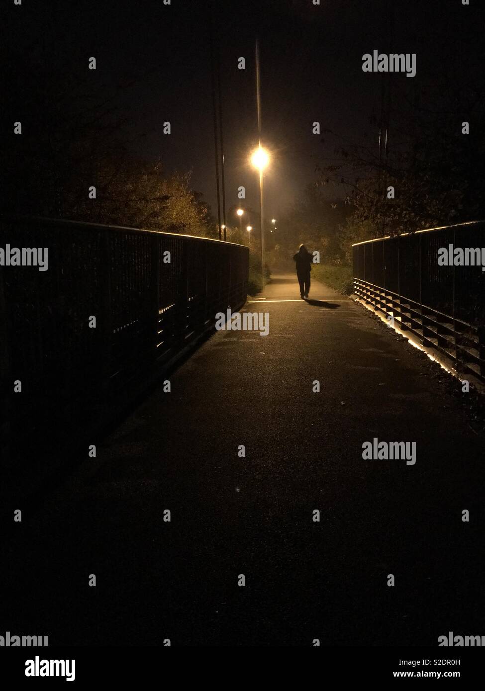 Uomo a piedi, verso un lampione, su un ponte di notte Foto Stock