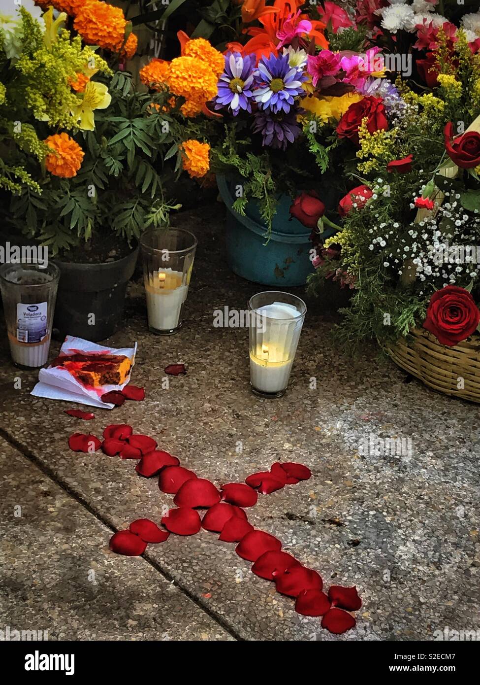 Una croce fatta dal rosso dei petali di rosa decora un recinto circondato da fiori freschi in onore di una persona cara a Día de los Muertos in Messico. Foto Stock