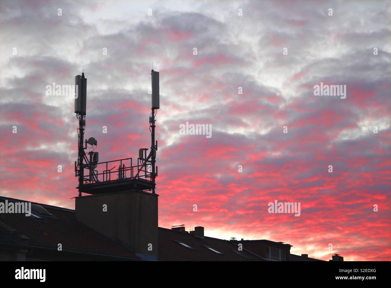 Tetto con montanti mobili e antenne nel tramonto colorato di rosso e nuvole Foto Stock