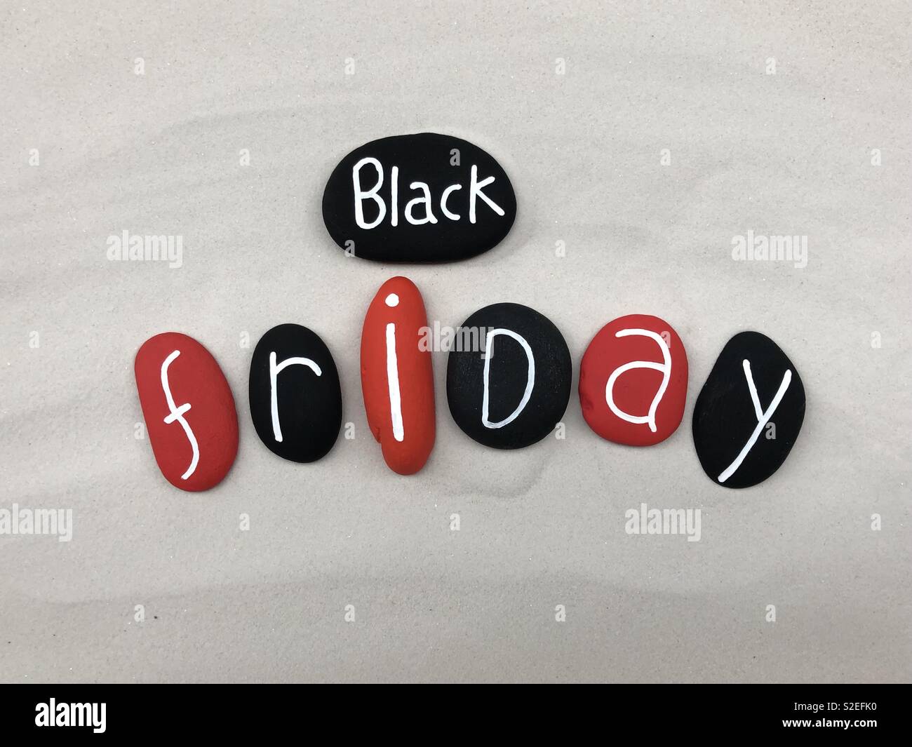 Venerdì nero con testo in bianco e nero e rosso con pietre colorate sulla sabbia bianca Foto Stock