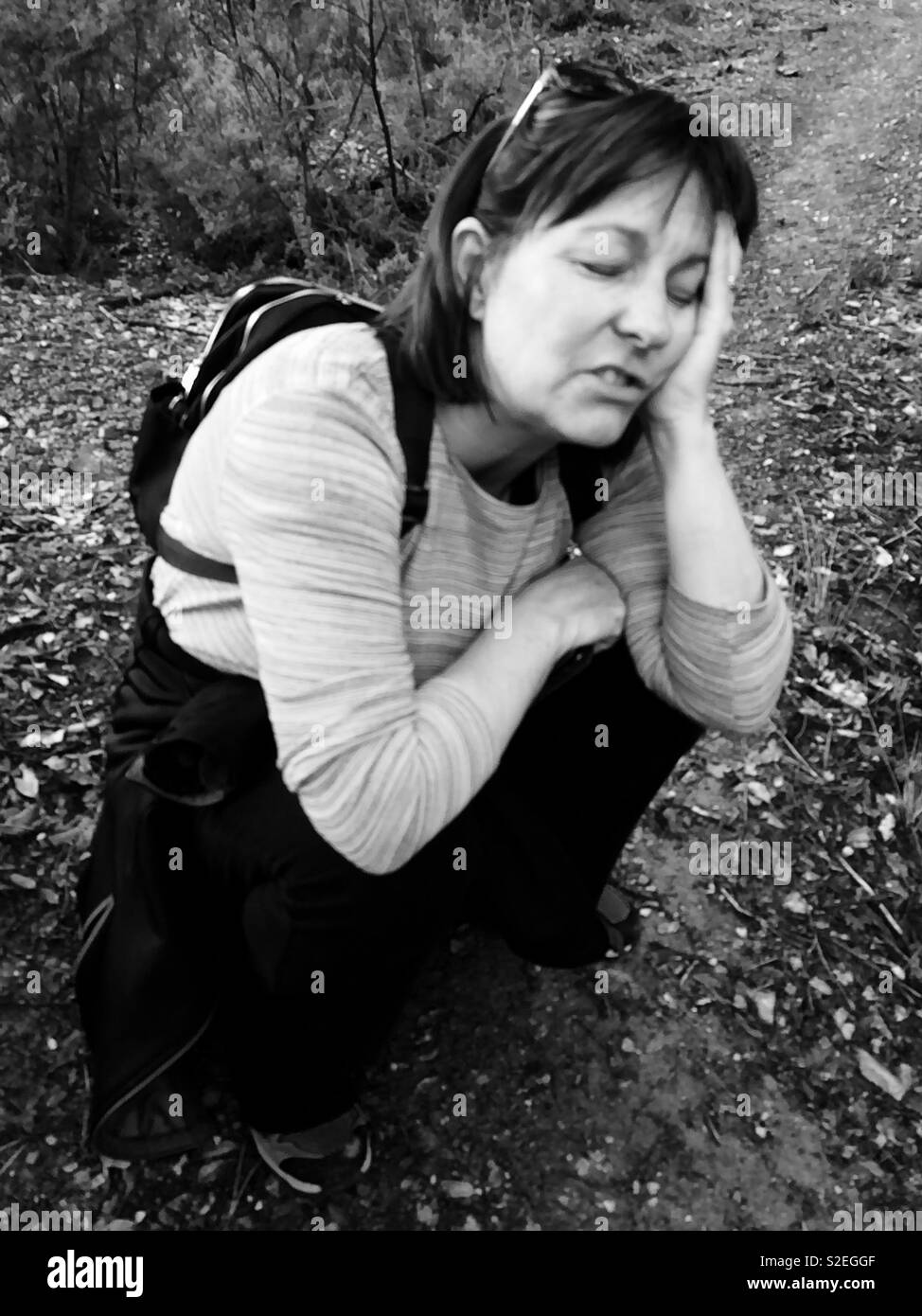 Donna escursionista da soli accovacciato sul terreno cercando stanco ed esausto dopo una lunga giornata di escursione Foto Stock