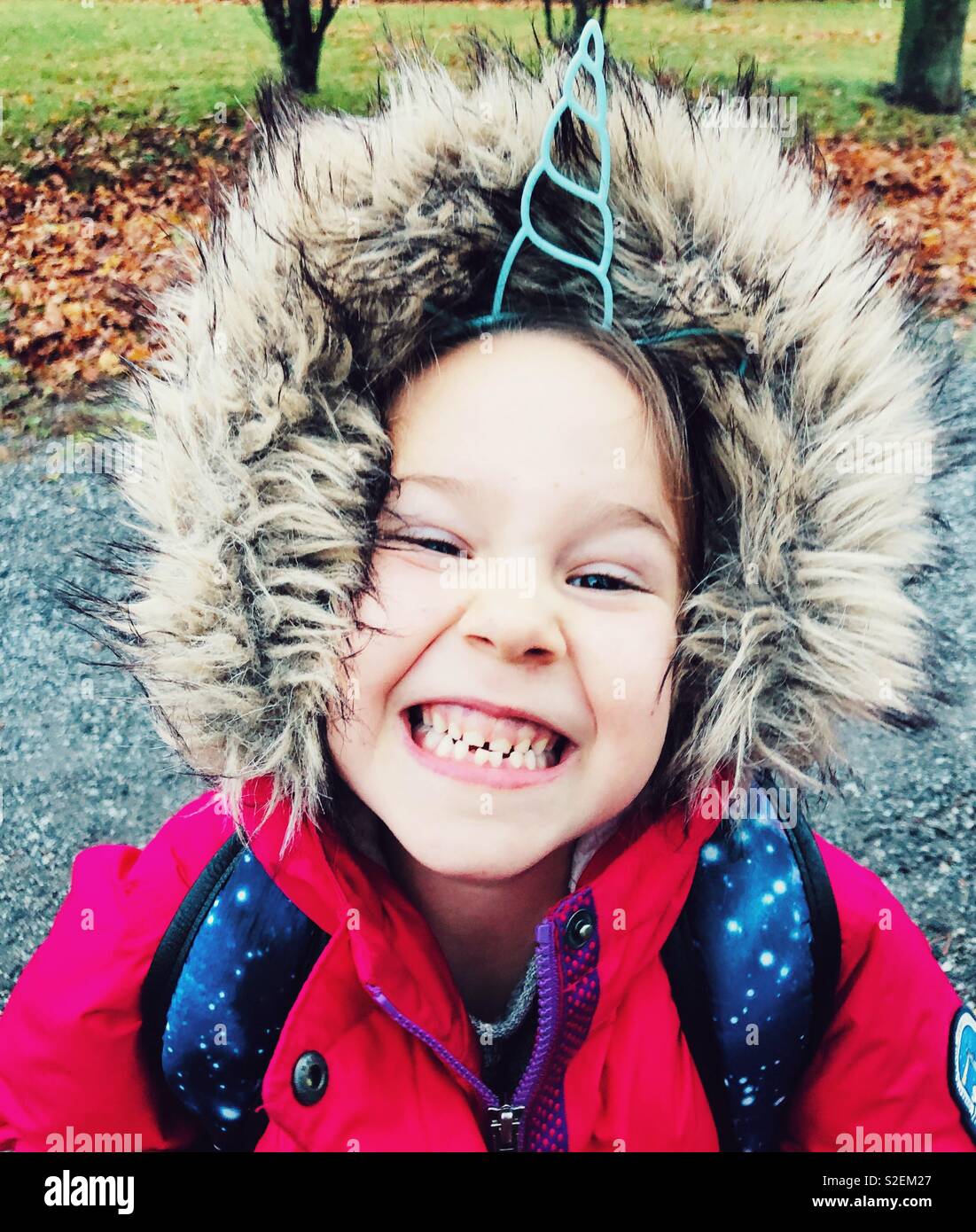 Ritratto di un sorridente 6 anno vecchia ragazza indossando di corno di unicorno archetto e rosa cappotto invernale con cappa di pelliccia - Immagine stock catturata con smartphone