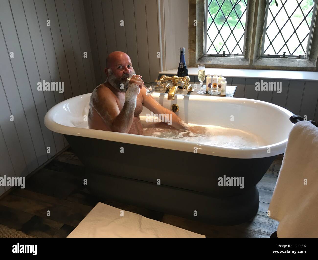 Uomo in vasca roll-top bevendo champagne Foto Stock