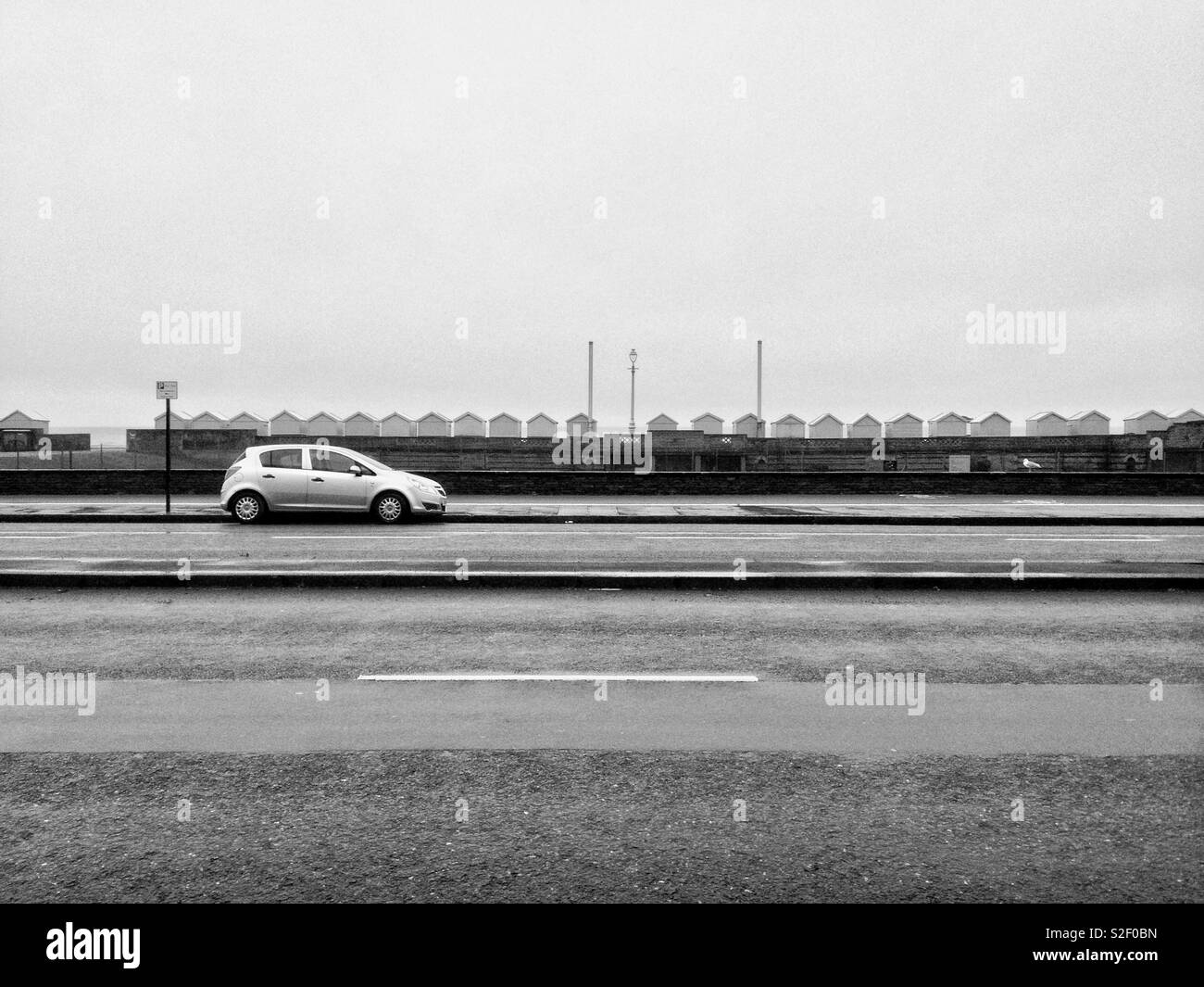 Una sola vettura parcheggiata su un deserto Kingsway davanti alla spiaggia di capanne dal lungomare Hove, East Sussex, su un livello di grigio e noiosa Domenica. - Immagine stock catturata con smartphone
