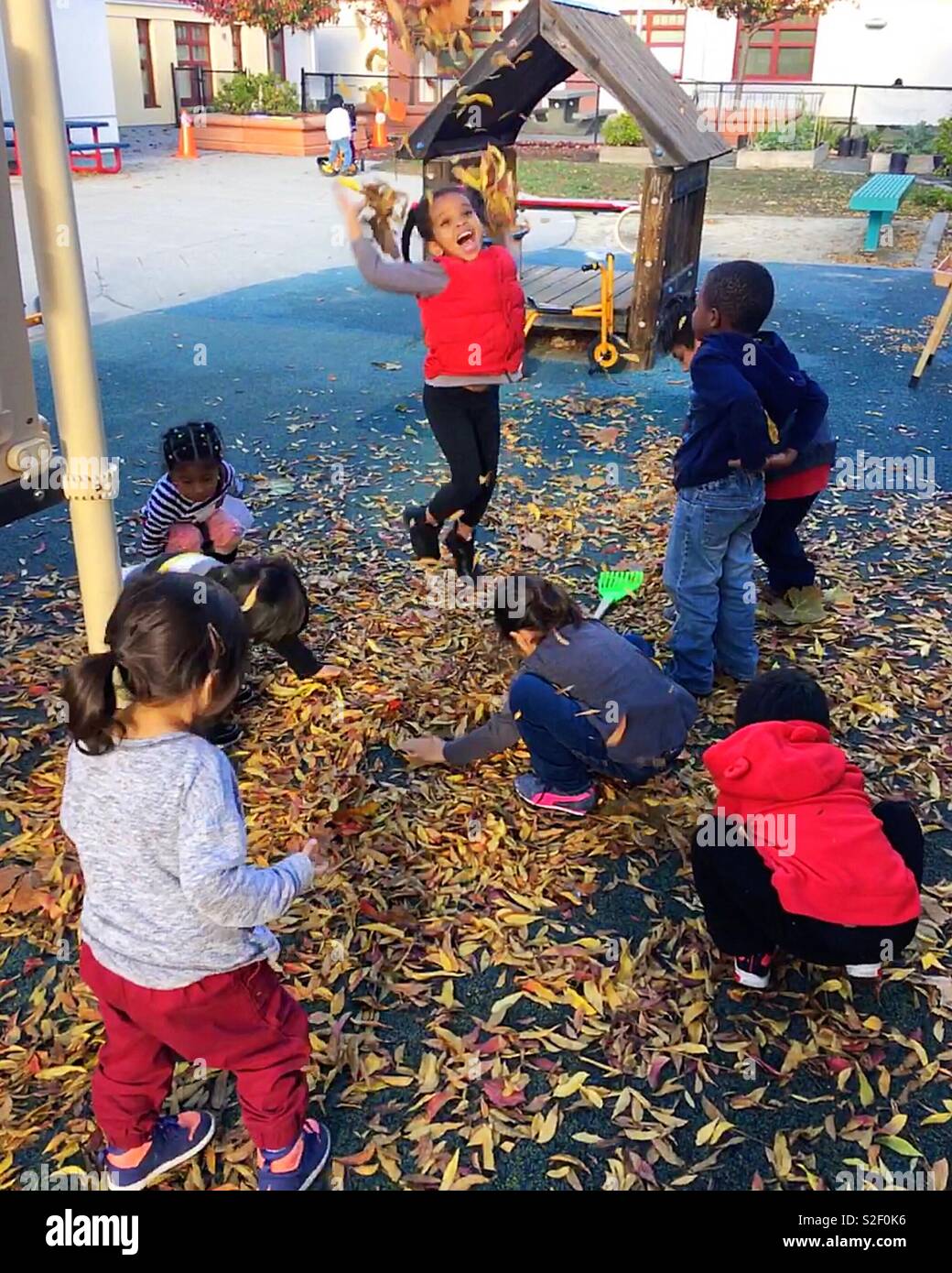 I bambini sono la riproduzione di foglie di autunno nel parco giochi e la ragazzina salta in alto con le sue mani di foglie di colore giallastro. Foto Stock