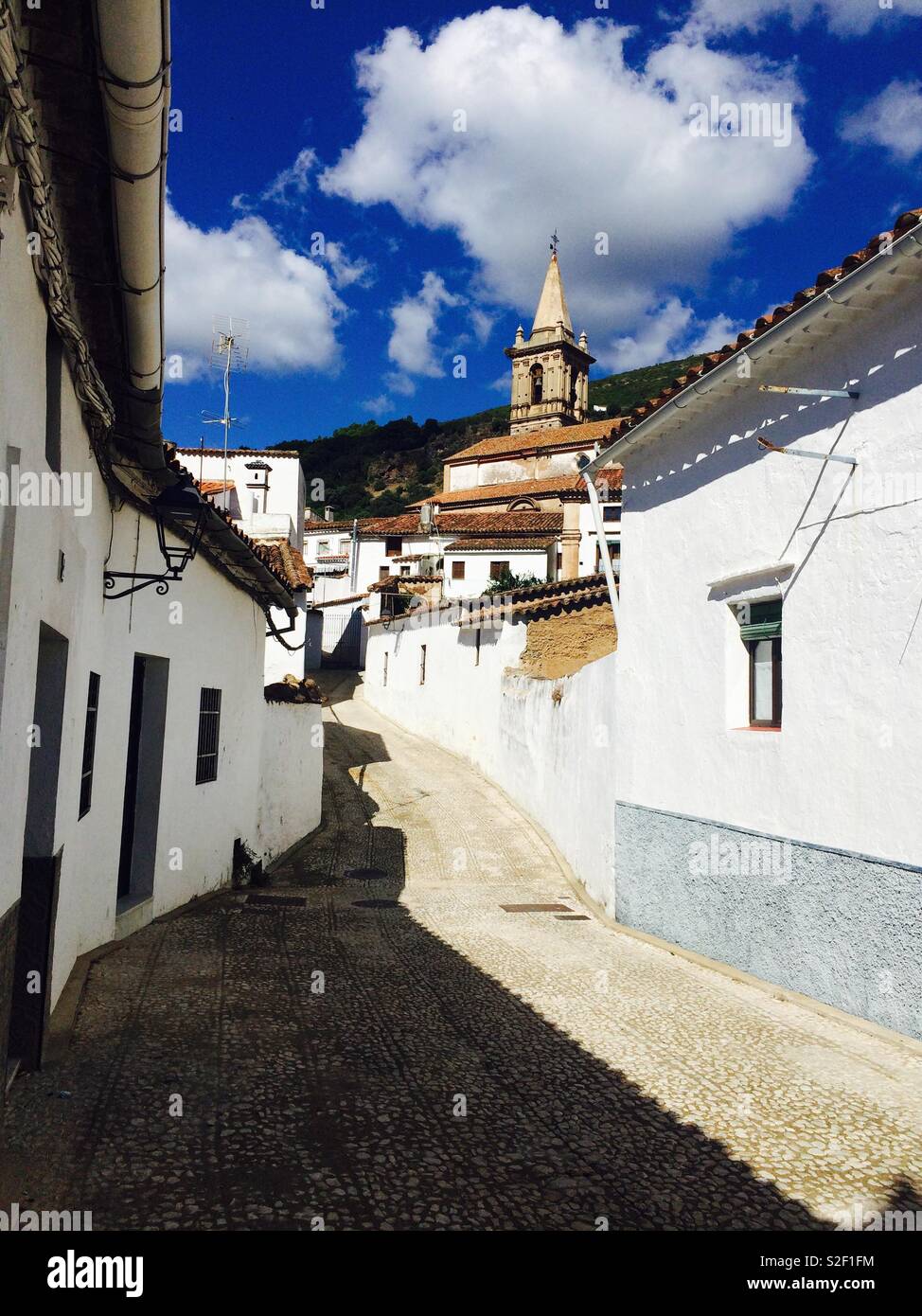 La ricerca di una stretta corsia o strada in un villaggio in Andalusia Spagna attraverso le vecchie case bianche e chiesa in cima alla collina - Immagine stock catturata con smartphone La ricerca di una stretta corsia o strada in un villaggio in Andalusia Spagna attraverso le vecchie case bianche e chiesa in cima alla collina - Immagine stock catturata con smartphone