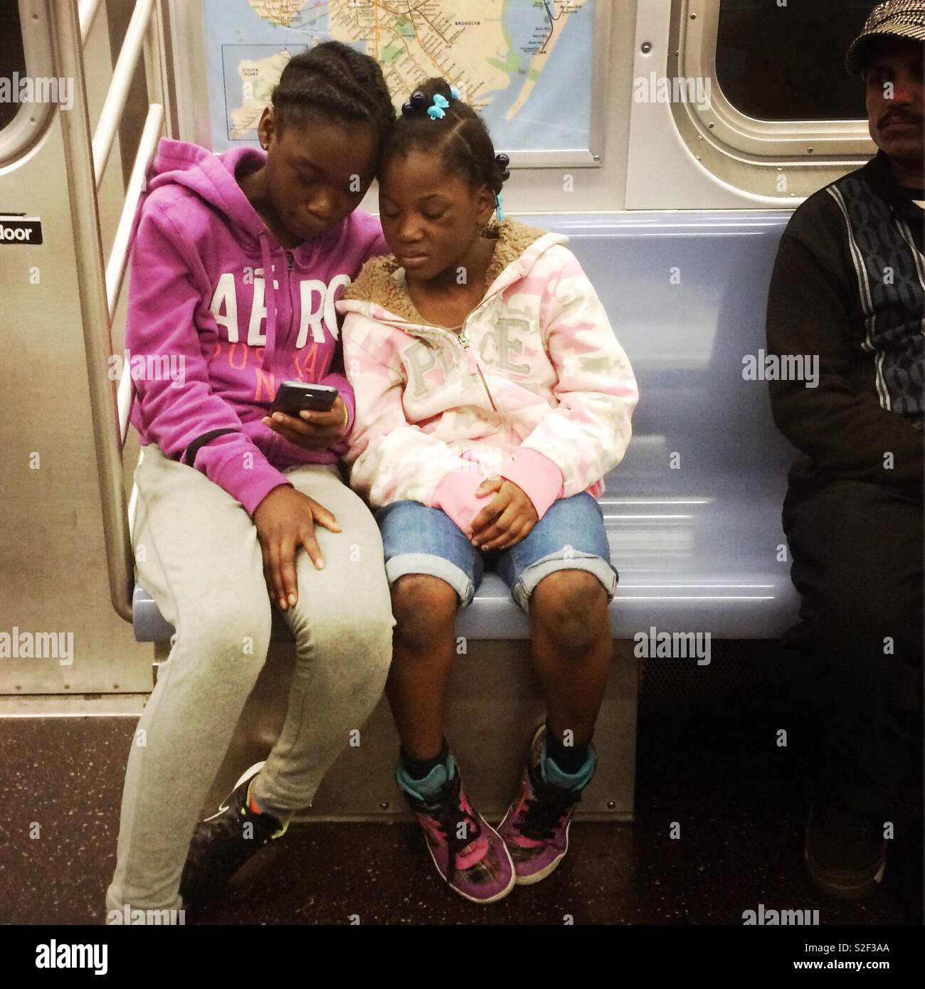 Sorelle guardando il loro telefono mobile insieme sulla metropolitana di nyc. Foto Stock