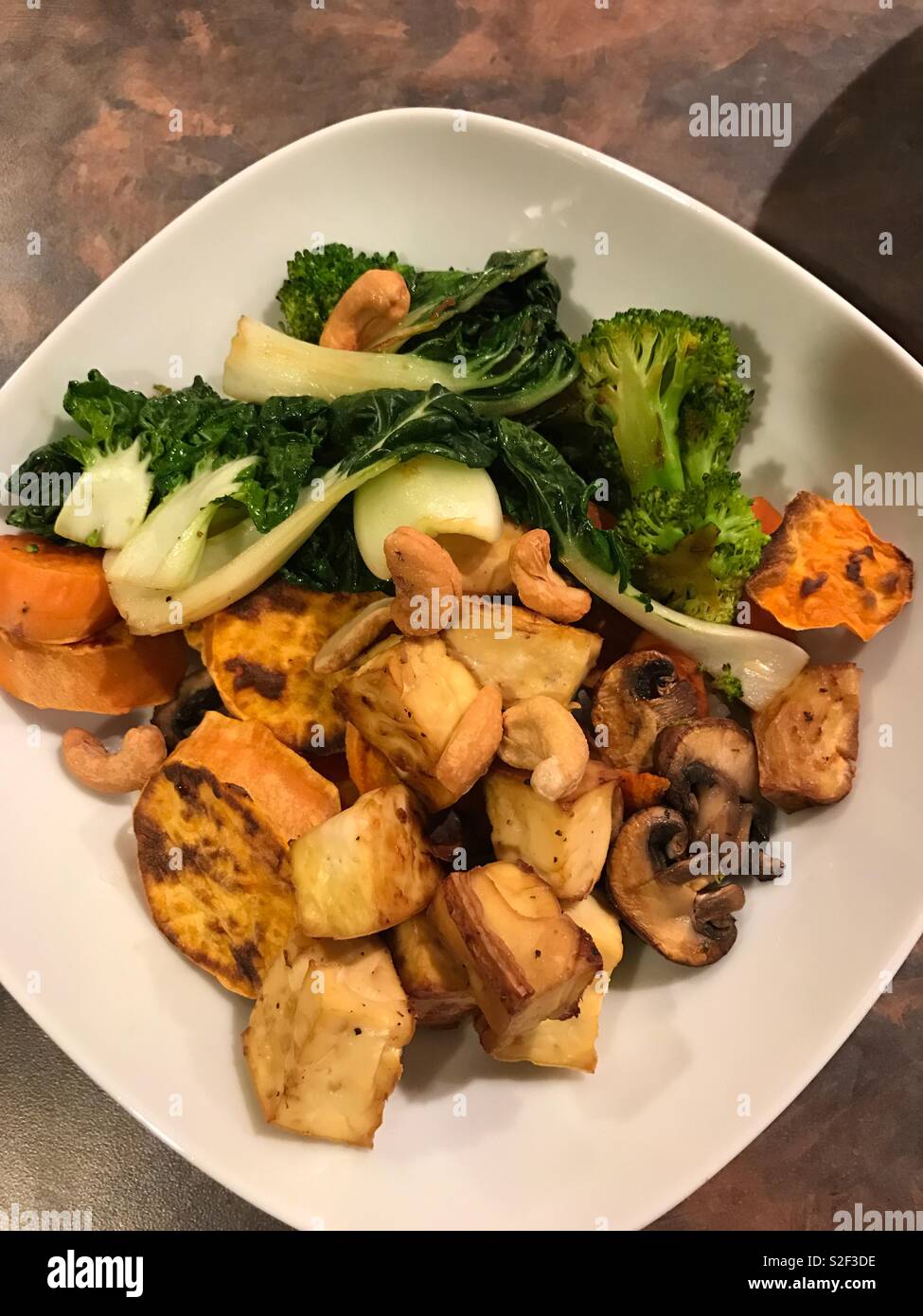 Deliziosi piatti vegan veggie ciotola con patate al forno e tofu, e sauté di broccoli, i funghi e i baby bok choy. - Immagine stock catturata con smartphone