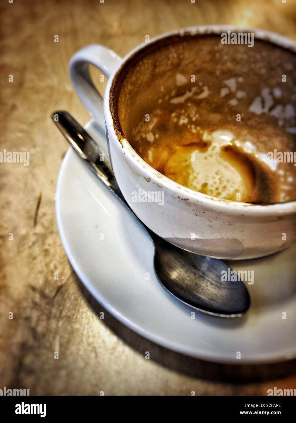 Guardando in basso una tazza di caffè vuota in un caffè dopo aver bevuto un caffè bianco piatto. Il manico della tazza e il cucchiaino sono allineati, le gocce del caffè sono visibili. - Immagine stock catturata con smartphone
