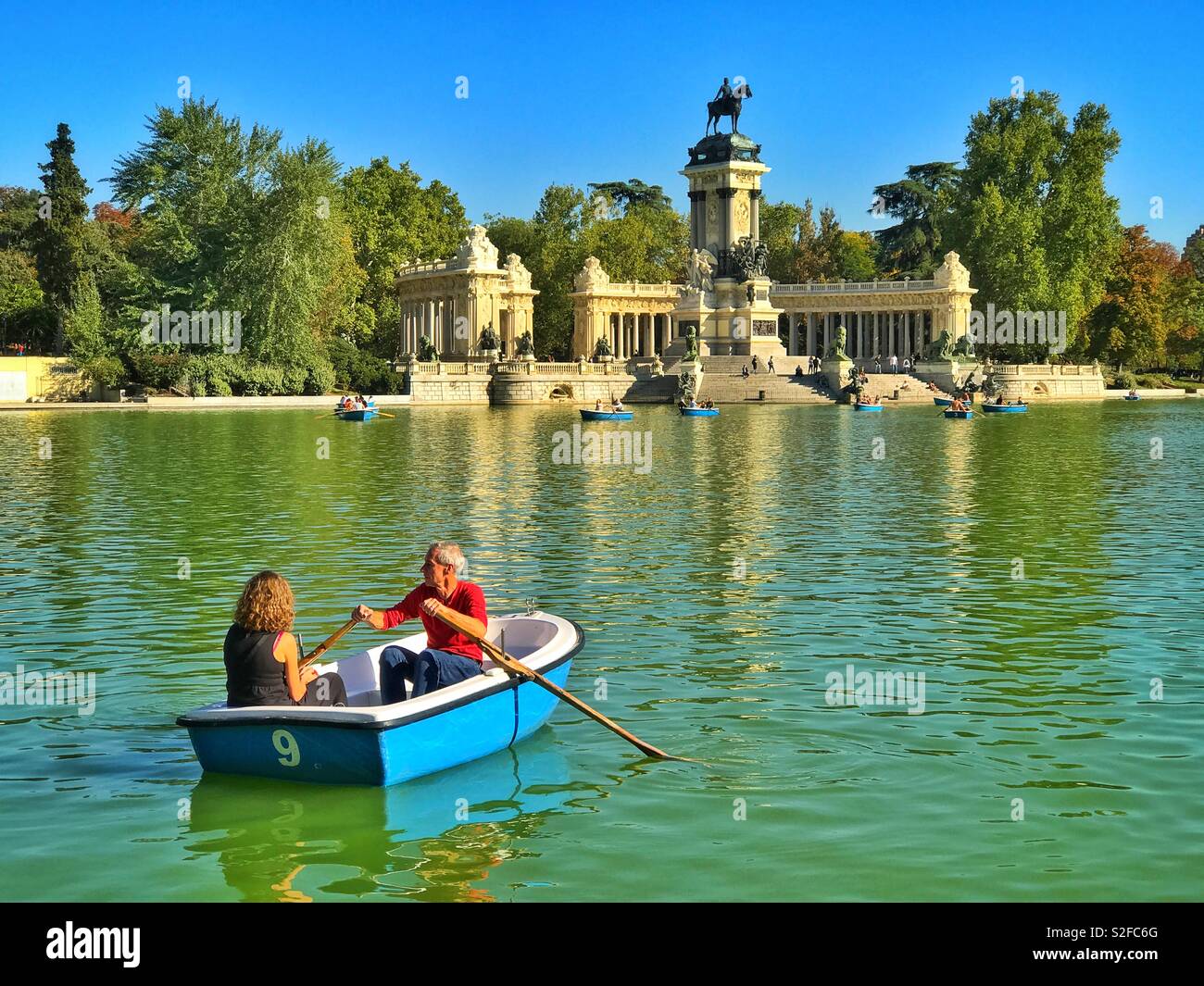 Due turisti pala in una barca sul lago del Parco del Buen Retiro di Madrid in Spagna. In fondo è il monumento ad Alfonso XII. Credito foto - © COLIN HOSKINS. - Immagine stock catturata con smartphone