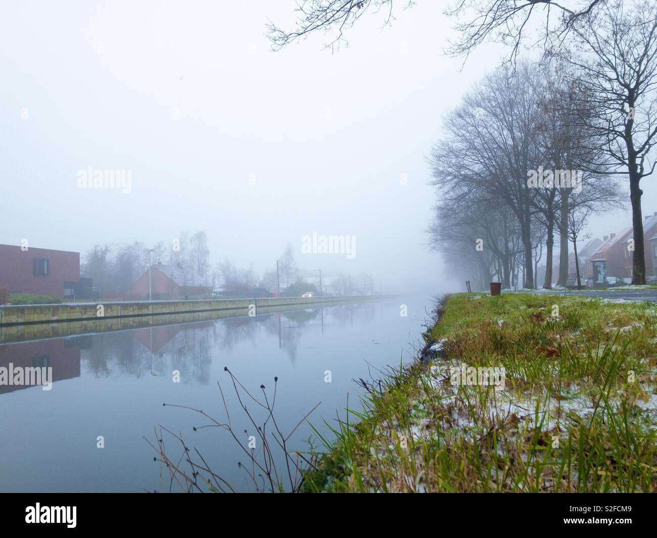 Giornata invernale sul lungofiume con la prima neve in erba sotto un grigio cielo nebbioso - Immagine stock catturata con smartphone