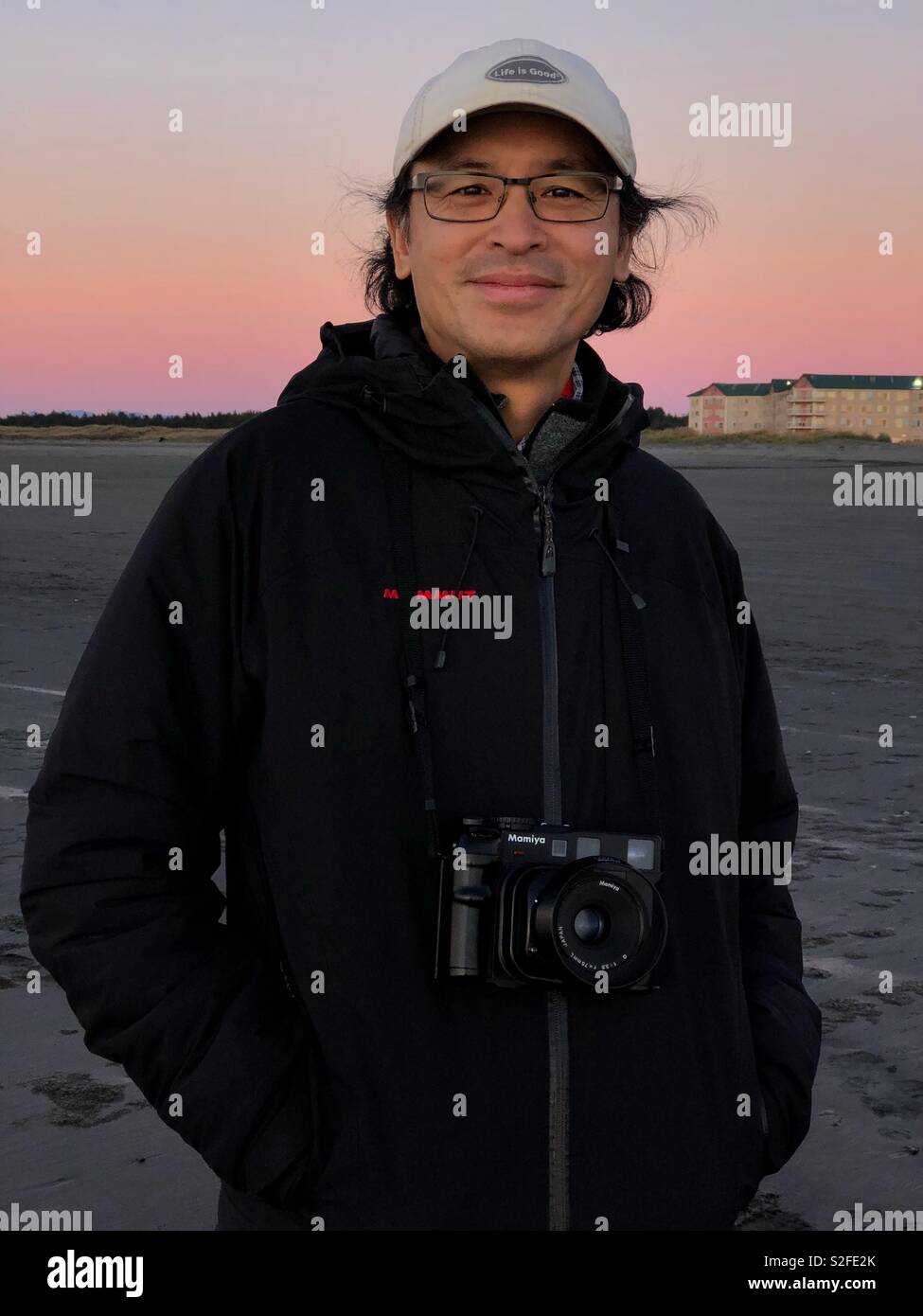 Sorridente uomo asiatico al tramonto con medio formato vintage Mamiya telecamera cinematografica - Immagine stock catturata con smartphone