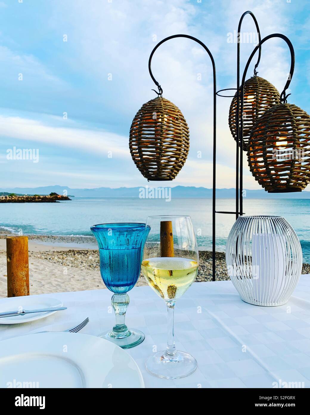 Tabella ristorante sulla spiaggia che si affaccia su un oceano di Punta Mita, Messico. Bicchieri di vino & luci pendenti. Foto Stock