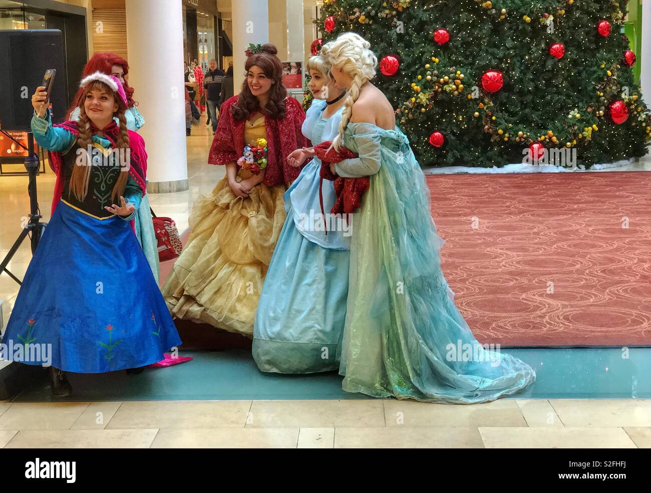 Principesse prendendo un selfie davanti a un gigantesco albero di Natale. Preso in un centro shopping mall, a Calgary, Alberta, Canada. Foto Stock