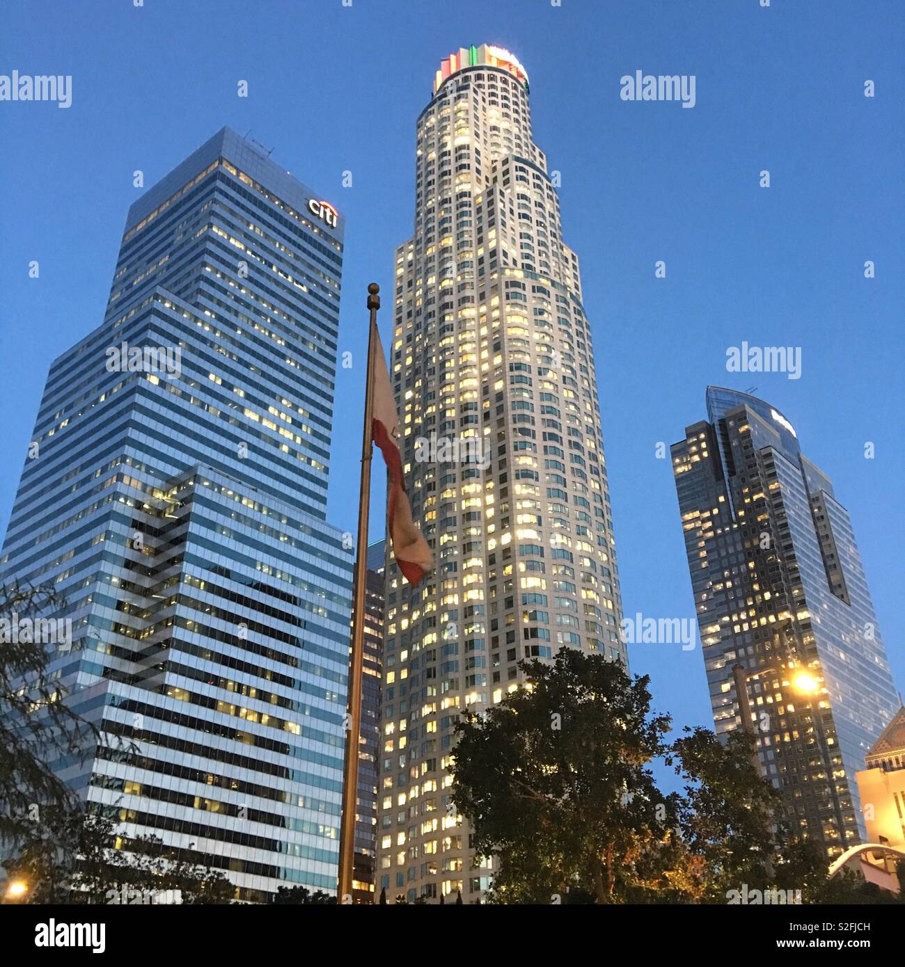 US Bank Tower, banca Citi e Deloitte grattacieli nel quartiere finanziario del centro cittadino di Los Angeles con la bandiera della California in primo piano al crepuscolo - Immagine stock catturata con smartphone