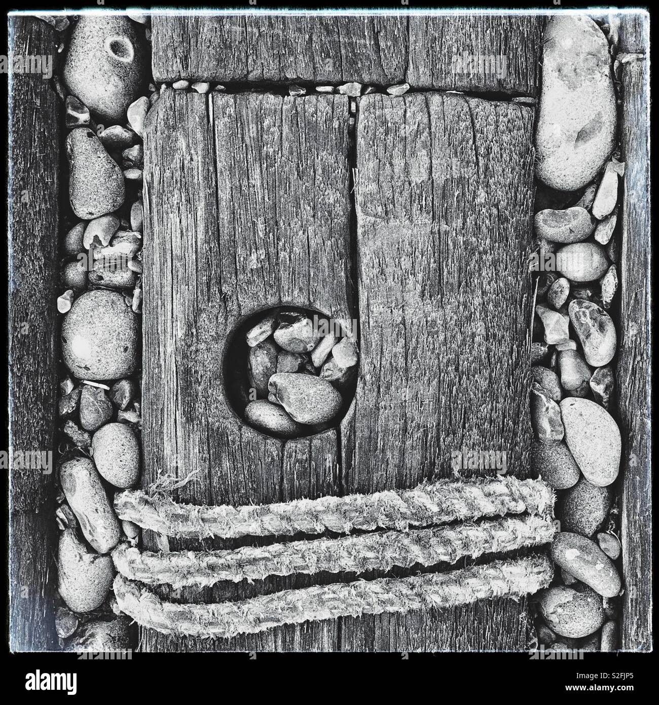 Corda allacciate intorno a un asse di legno circondato da ciottoli in monocromia Foto Stock