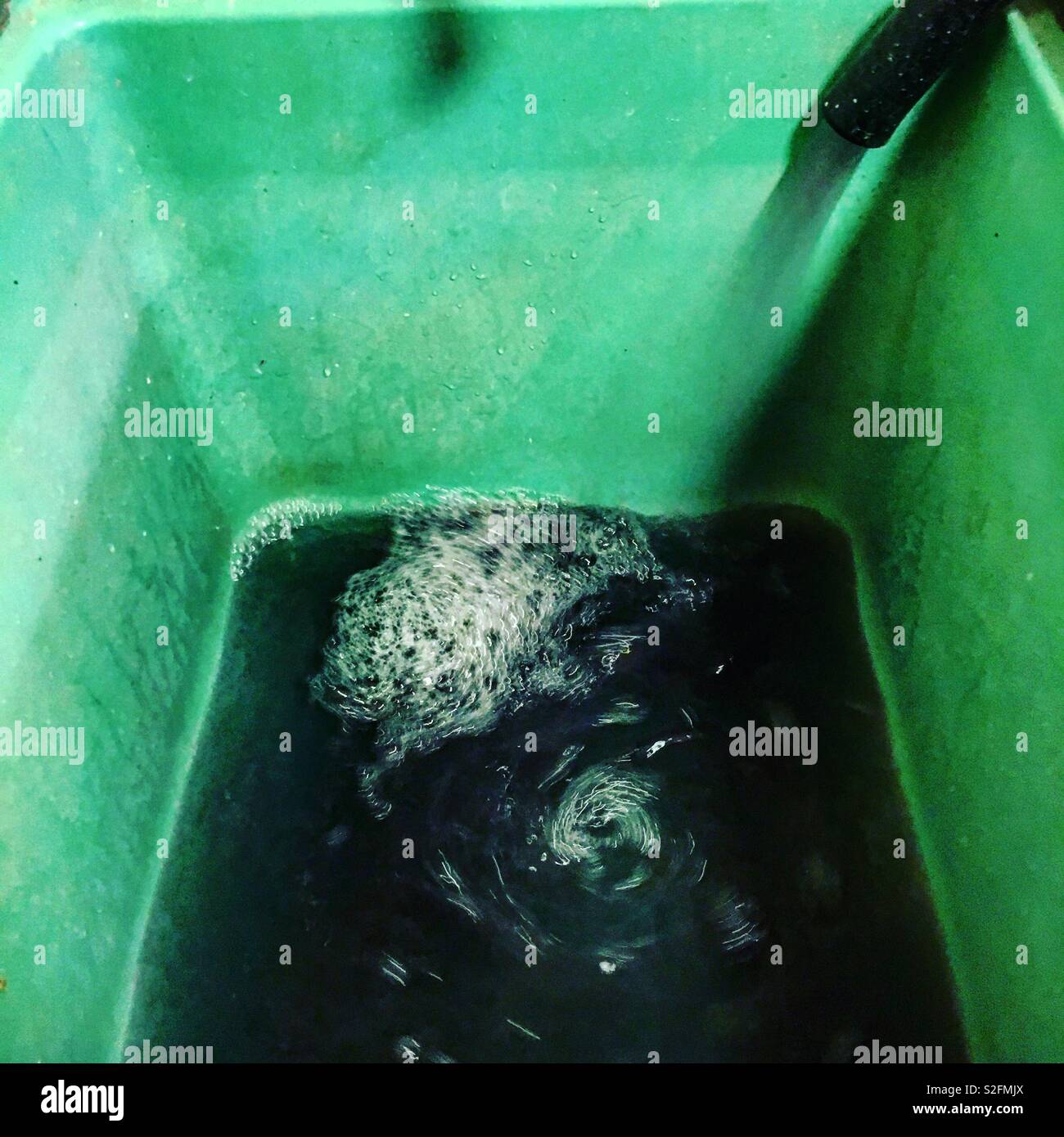Verde servizio lavanderia vasca essendo riempito con acqua annerito dal lavaggio di colorante fuori dai nuovi vestiti. Foto Stock