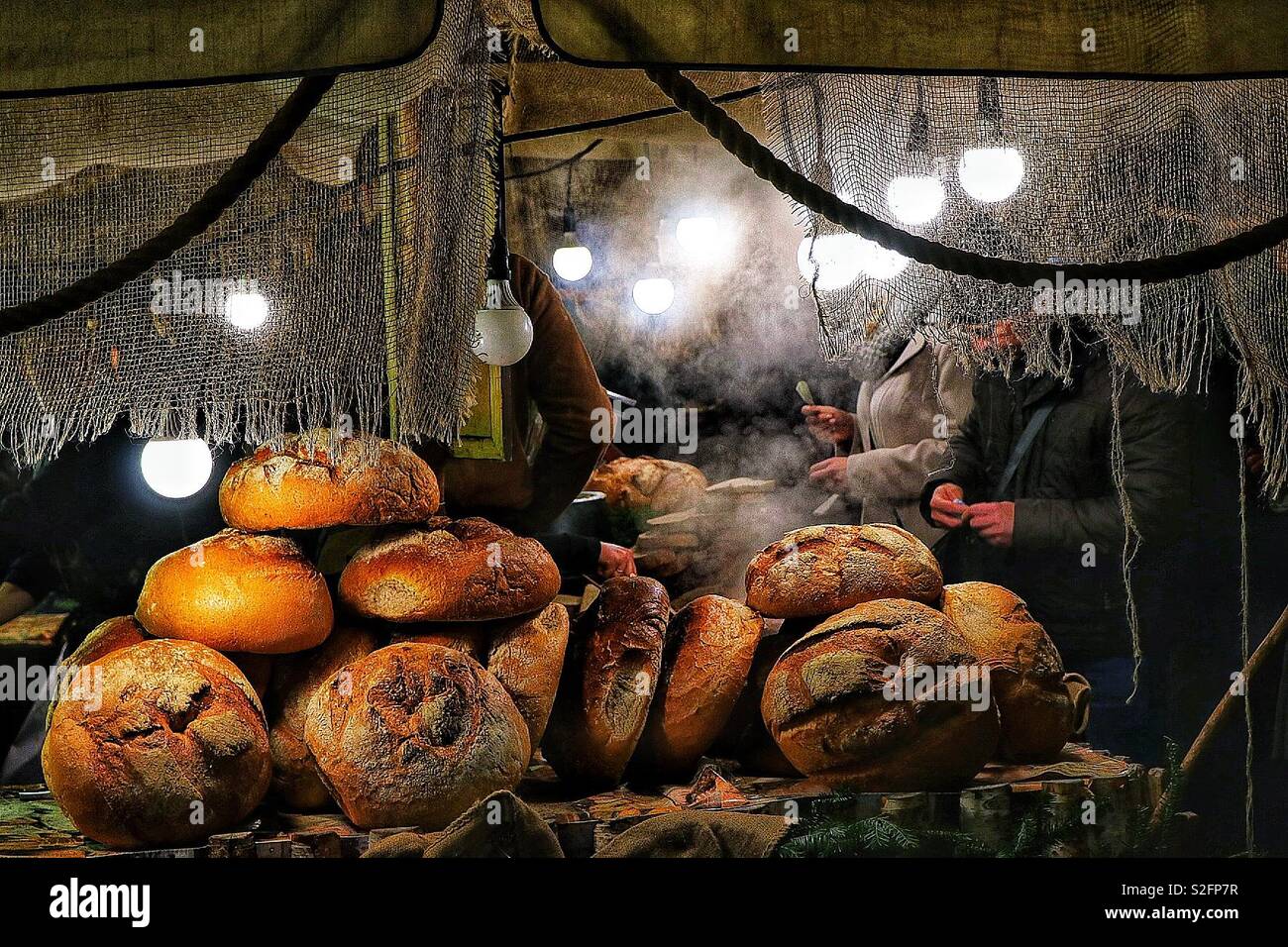 Un chiosco di cibo al mercato di Natale di Cracovia vende pane e cibi caldi, creando un'atmosfera di vacanza calda e accogliente con prelibatezze tradizionali polacche - Immagine stock catturata con smartphone