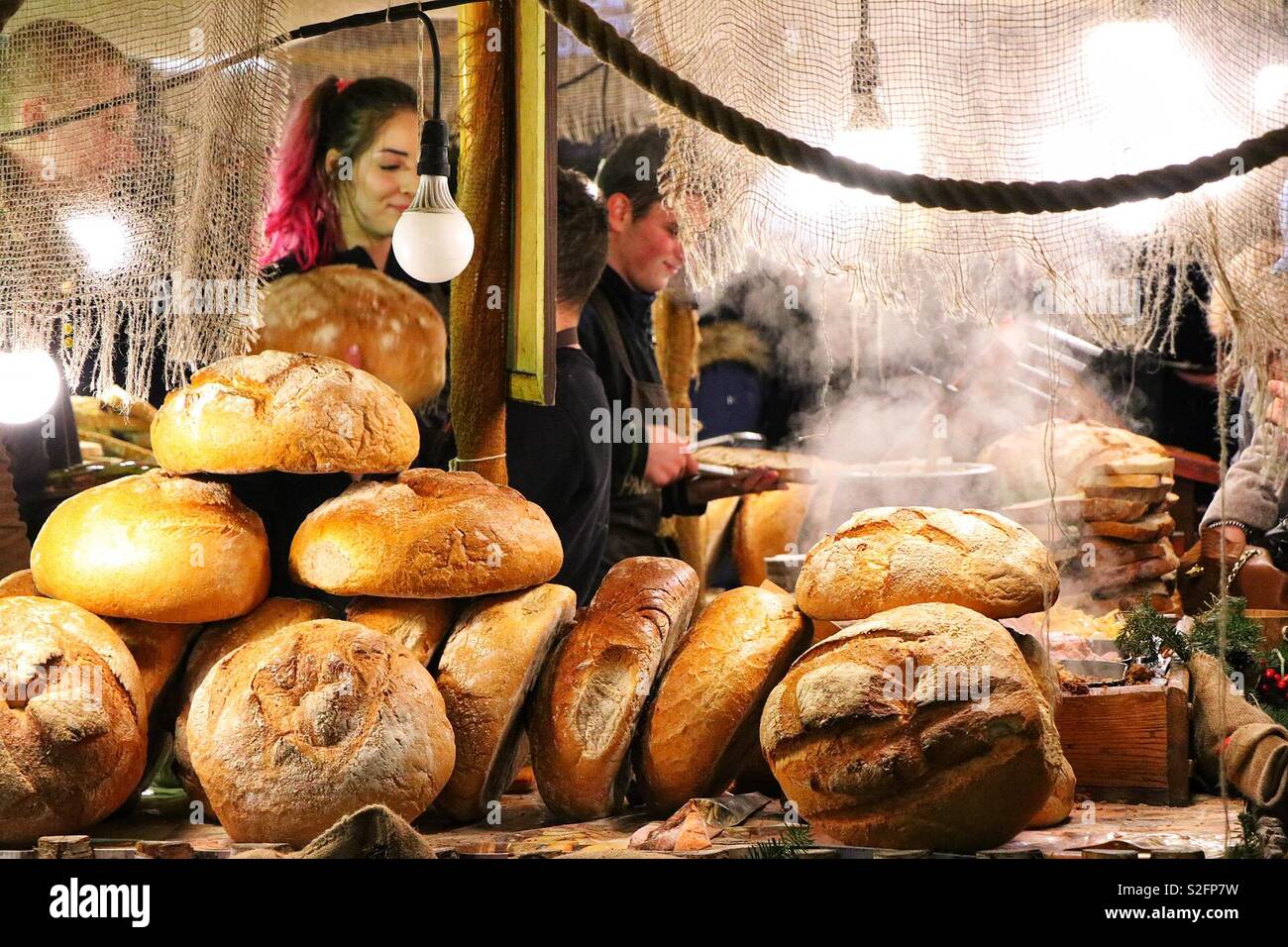 Un chiosco di cibo al mercato di Natale di Cracovia vende pane e cibi caldi, creando un'atmosfera di vacanza calda e accogliente con prelibatezze tradizionali polacche - Immagine stock catturata con smartphone