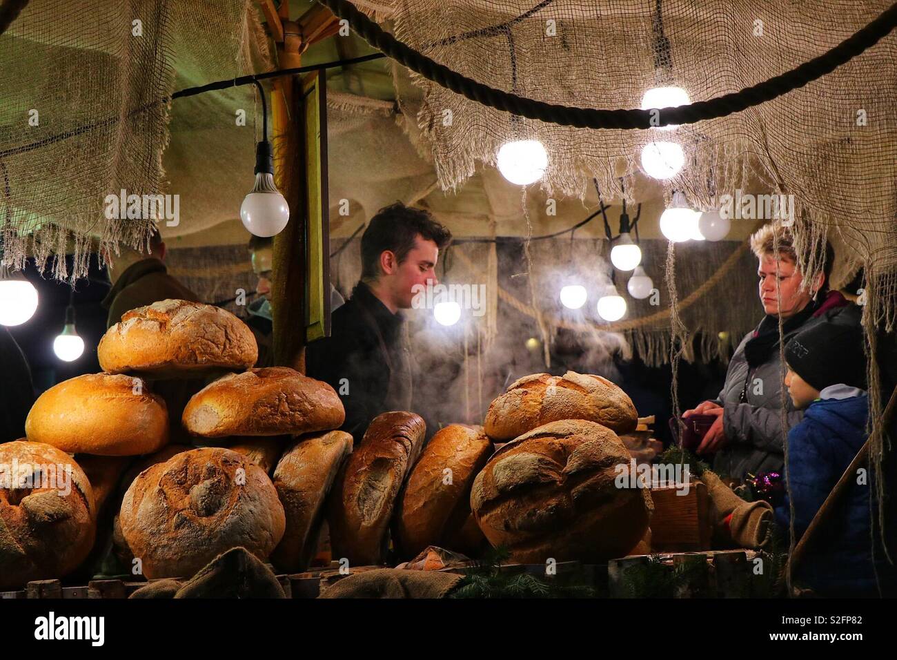 Un chiosco di cibo al mercato di Natale di Cracovia vende pane e cibi caldi, creando un'atmosfera di vacanza calda e accogliente con prelibatezze tradizionali polacche - Immagine stock catturata con smartphone
